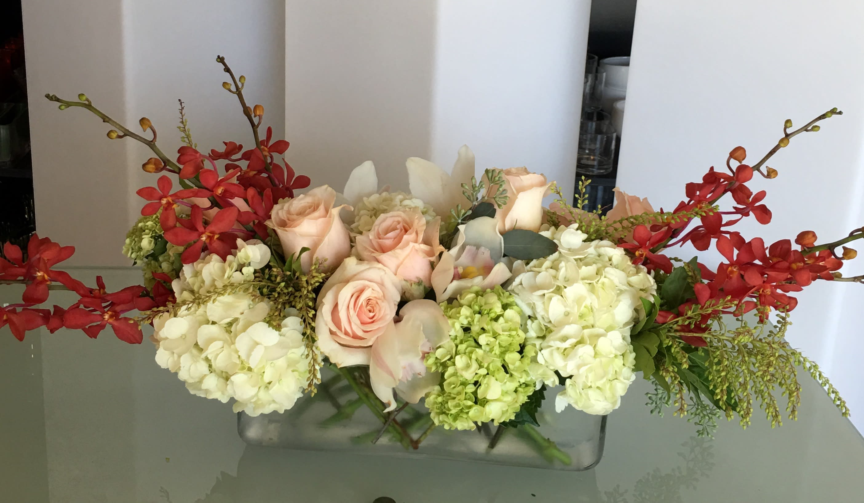 Arrangement of peach roses and white hydrangeas with red orchids in a glass vase