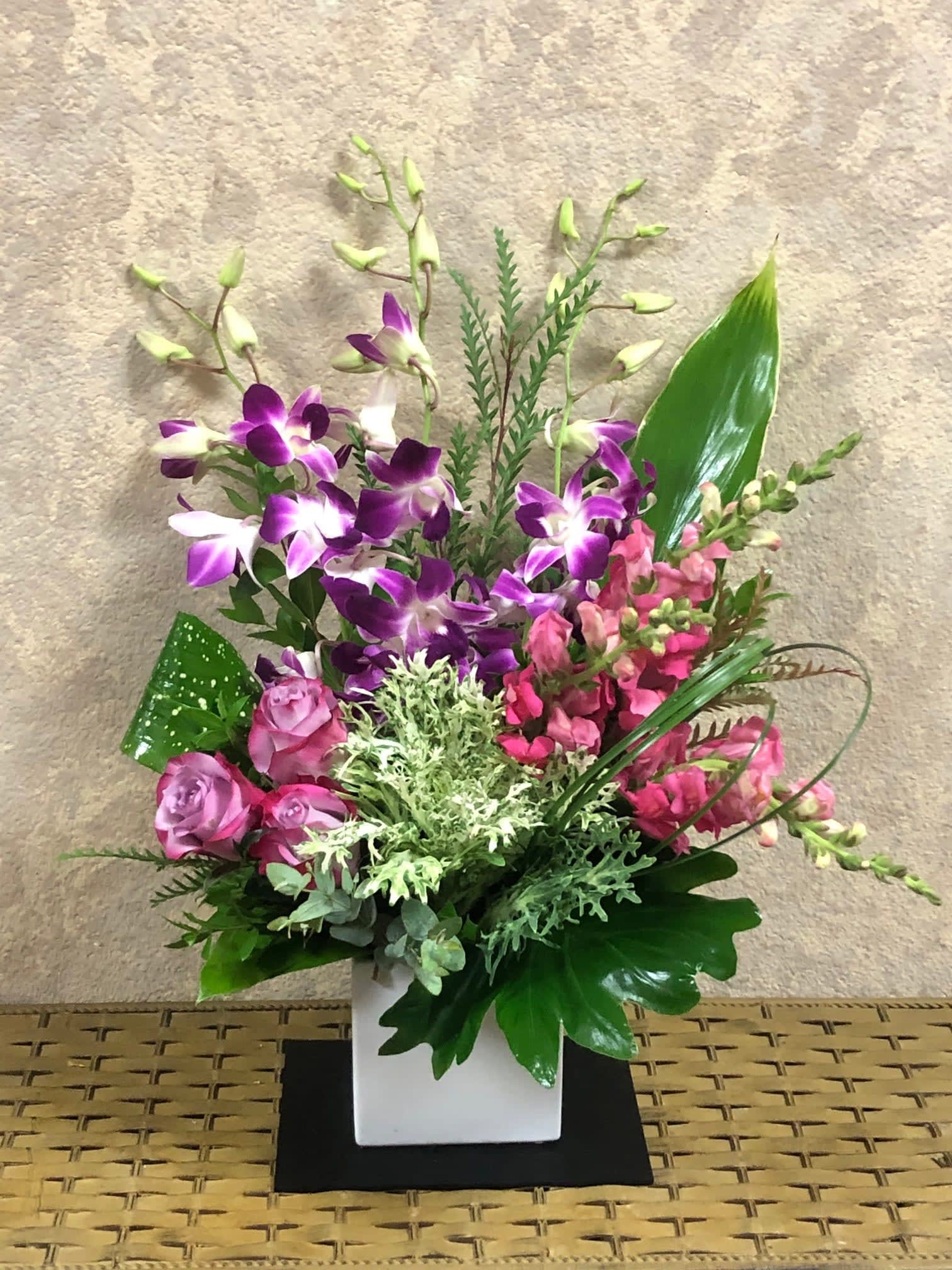 Purple orchids and pink flowers arranged in a white square vase