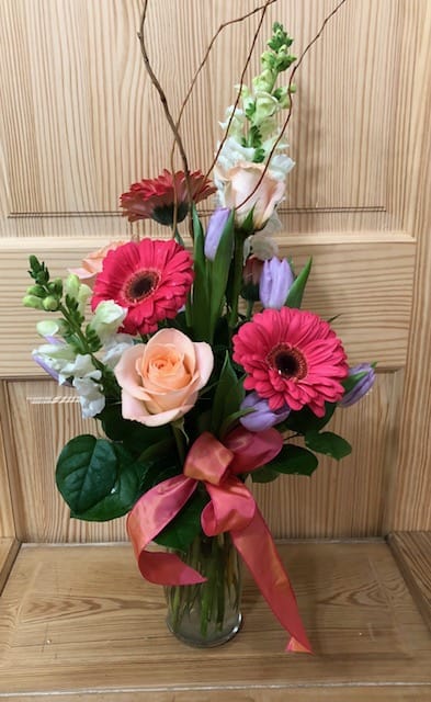 Mixed bouquet with pink gerberas, a peach rose, and purple tulips in a glass vase
