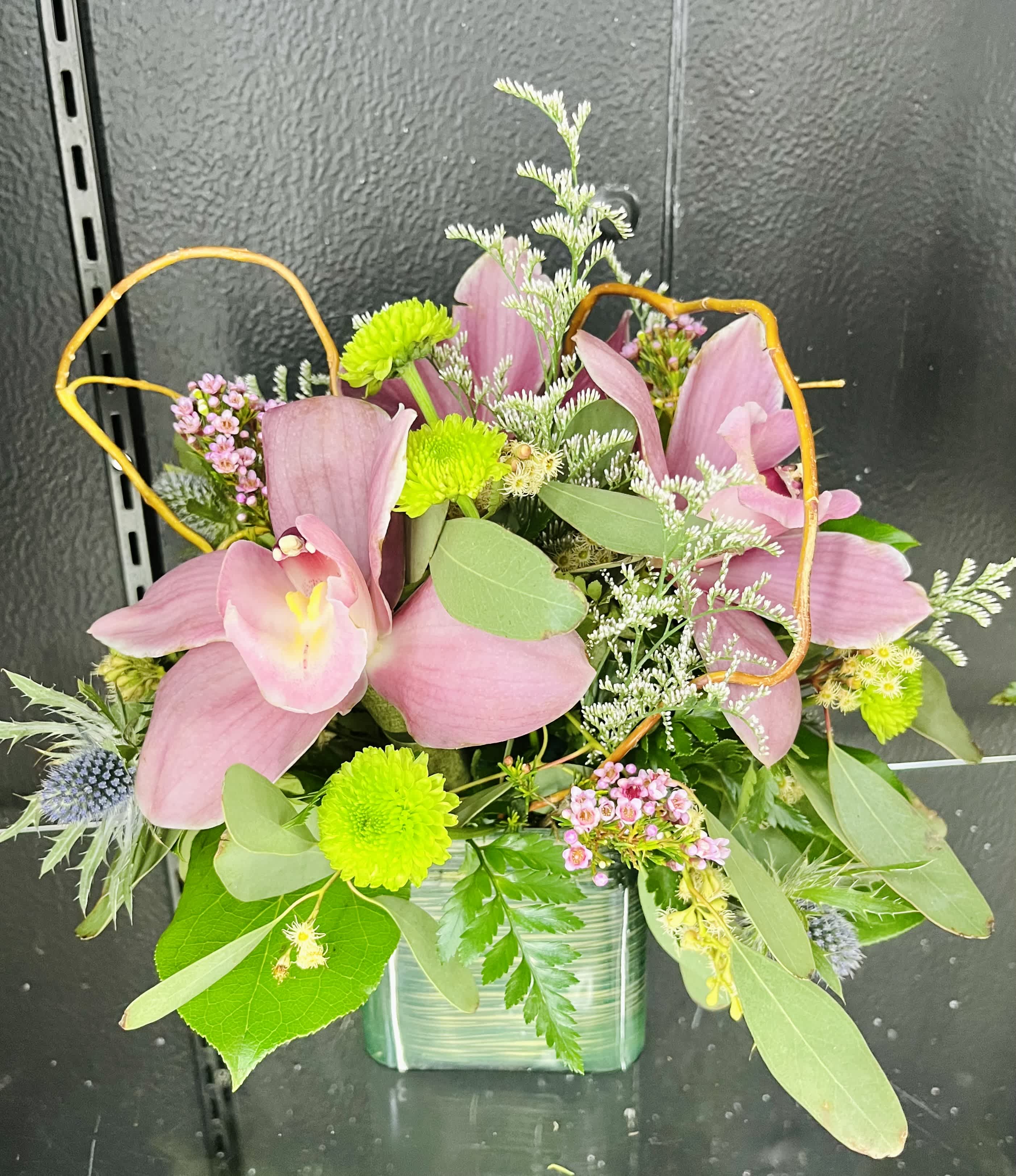 Compact arrangement of pink lilies and green button mums in a green glass cube vase