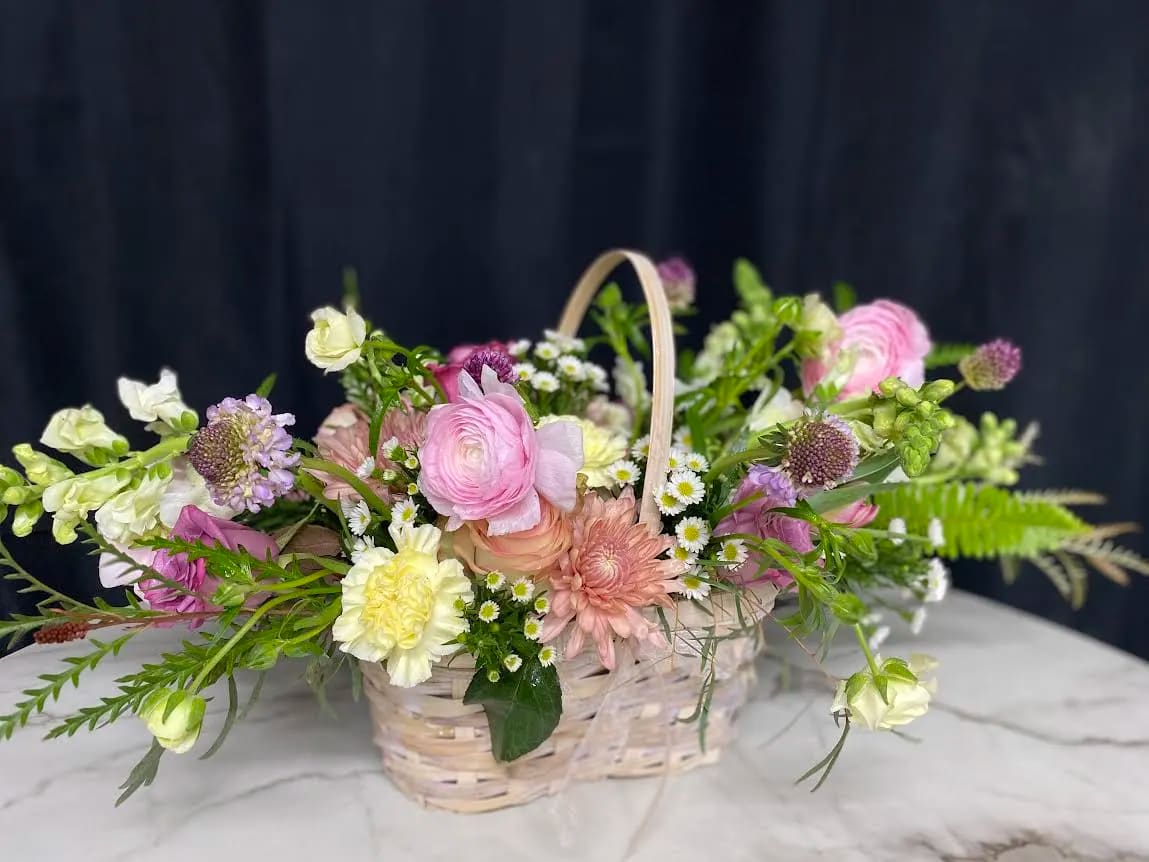 Pastel mixed flower arrangement in a wicker basket with a handle