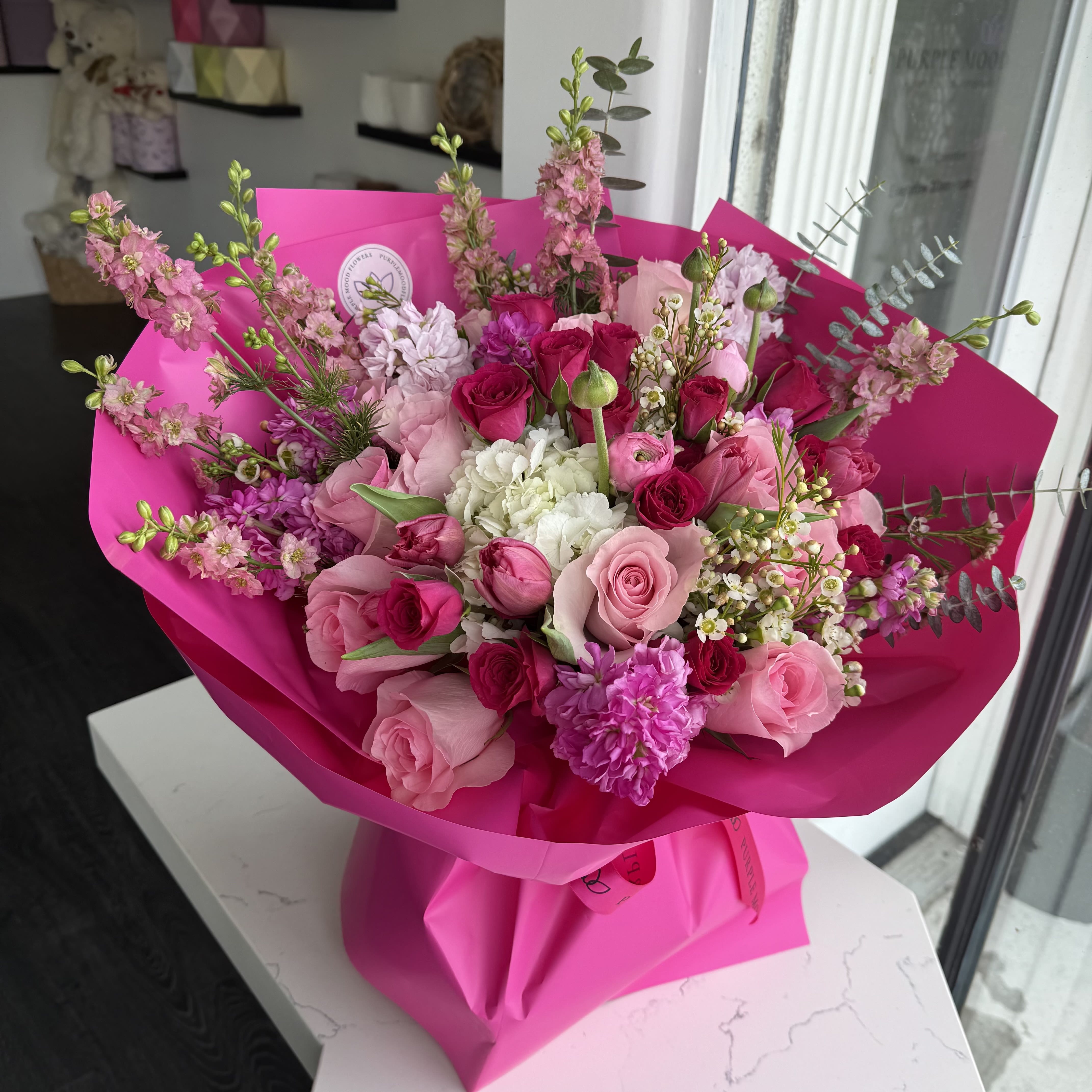 Bombita Bouquet - Vibrant, bold, and bursting with personality — our Bombita Bouquet is a lively mix of premium pink roses, tulips, carnations, and seasonal blooms. Designed in shades of hot pink, blush, and cream, it’s wrapped in striking fuchsia paper for a modern, statement-making look. Perfect for celebrating life’s happiest moments or gifting a burst of joy.    •    Premium roses, tulips, carnations, and seasonal fillers     •    A bold mix of pink tones, from blush to hot pink     •    Hand-wrapped in bright fuchsia paper with ribbon finish     •    Represents joy, love, and celebration     •    Perfect for birthdays, congratulations, or “just because”  VASE NOT INCLUDED