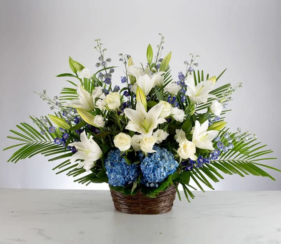 Deepest Condolences by BloomNation™ - A blue, white, and green funeral basket for any type of service. Held in a wicker basket, large palms spread out and give a natural spotlight for the feature blooms and colors.