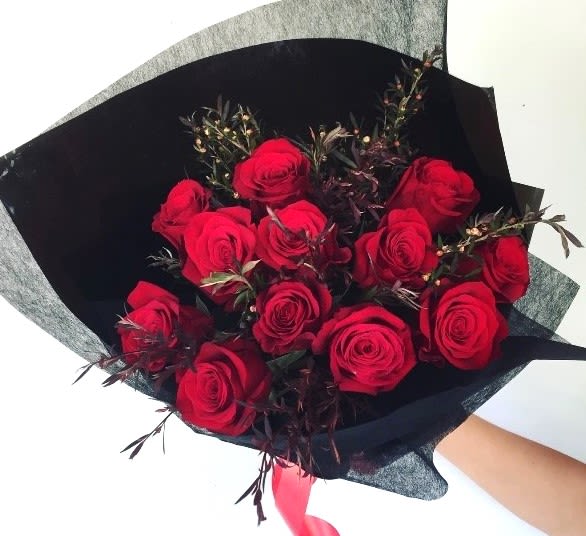 Bouquet of red roses wrapped in black paper with a pink ribbon