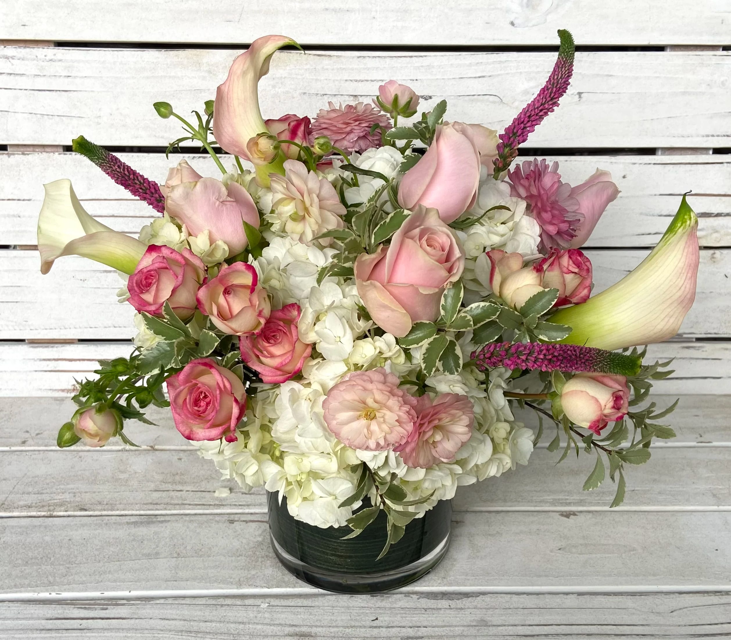 Low pink and white bouquet with roses, calla lilies, and hydrangeas in a glass cylinder vase