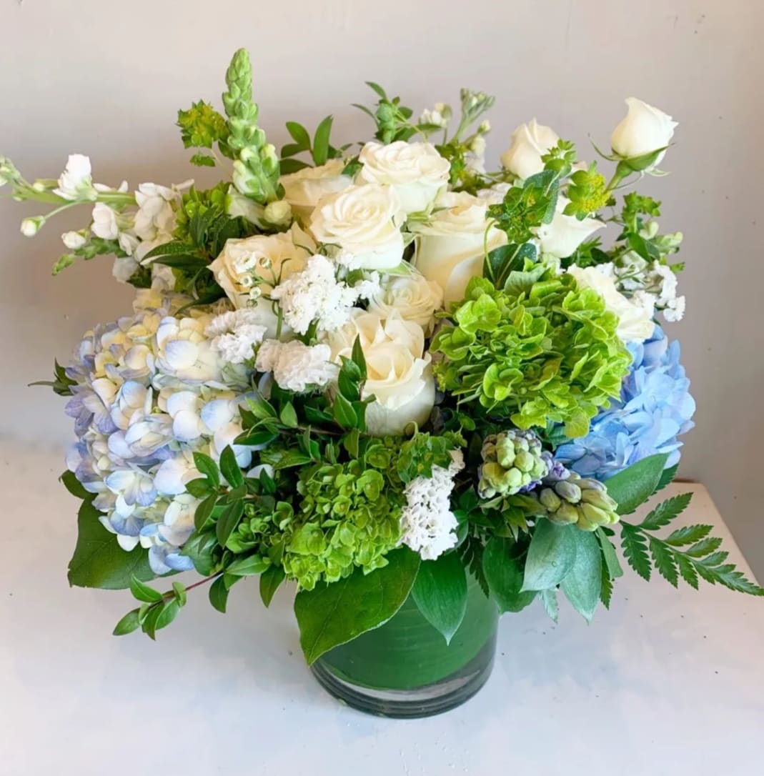 White roses and blue hydrangeas in a green glass vase