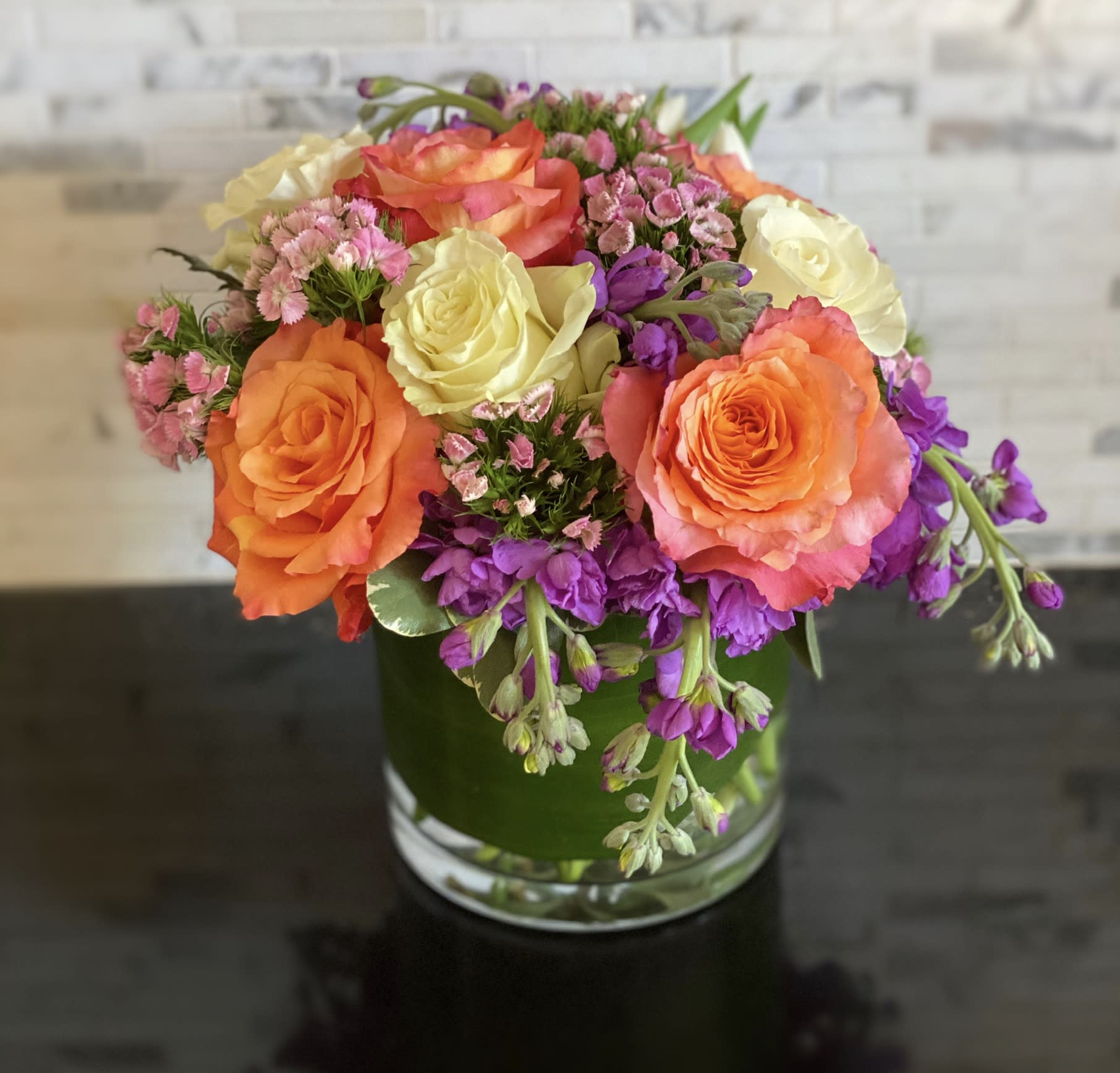 Bouquet of orange, yellow, and purple flowers in a glass vase