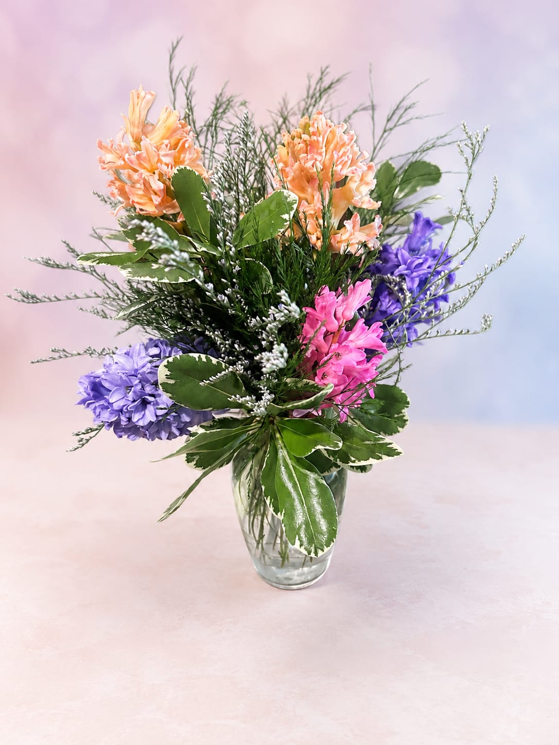 Pastel Meadow Breeze - Soft, airy, and full of cheerful color, Pastel Meadow Breeze features a whimsical mix of peach, lavender, pink, and violet blooms gathered with flowing greenery and delicate filler flower accents. Designed in a clear glass vase, this arrangement brings a fresh garden-inspired feel that’s perfect for birthdays, thinking of you moments, spring celebrations, or simply brightening someone’s day with a touch of pastel charm.