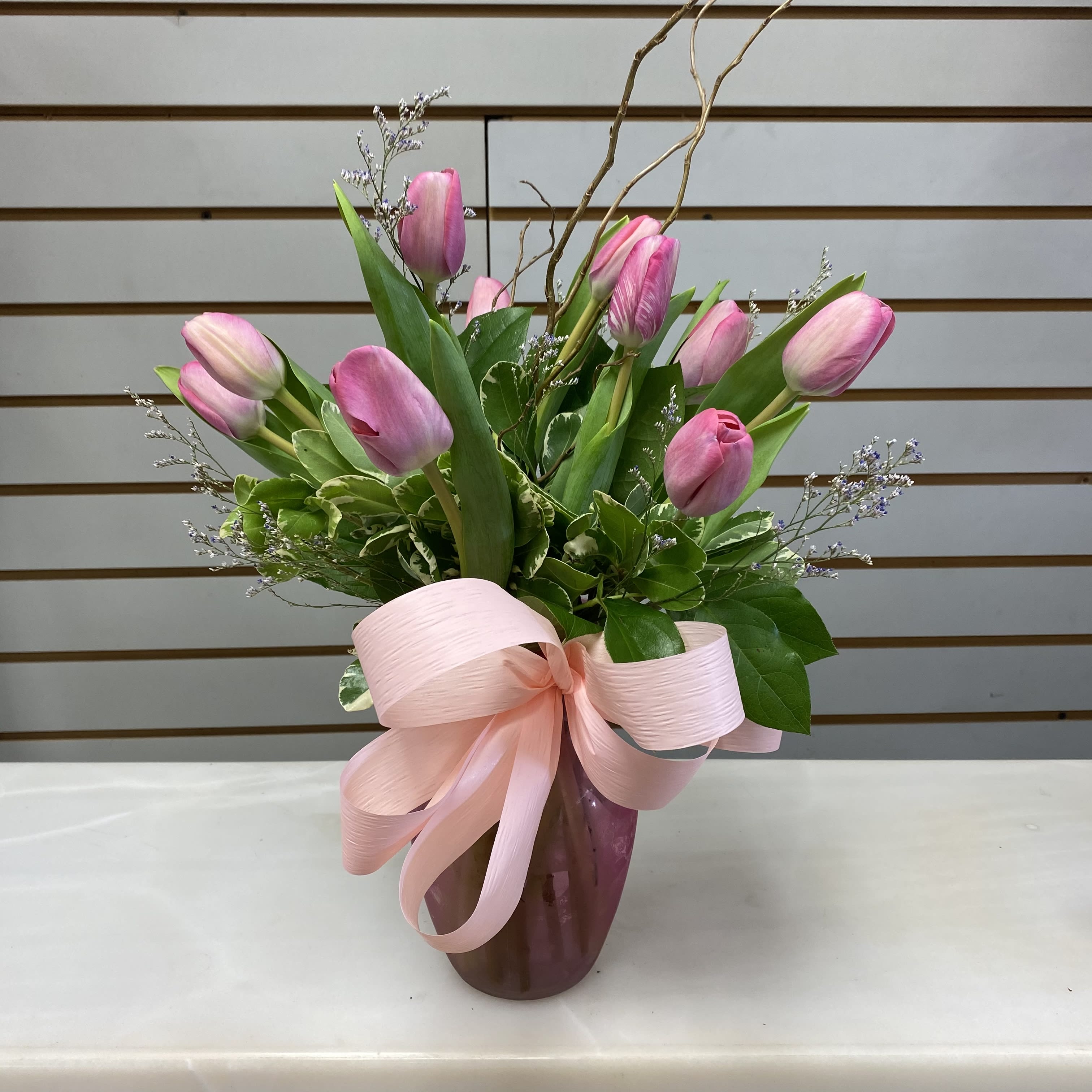 Pink tulips arranged in a vase with a large pink ribbon