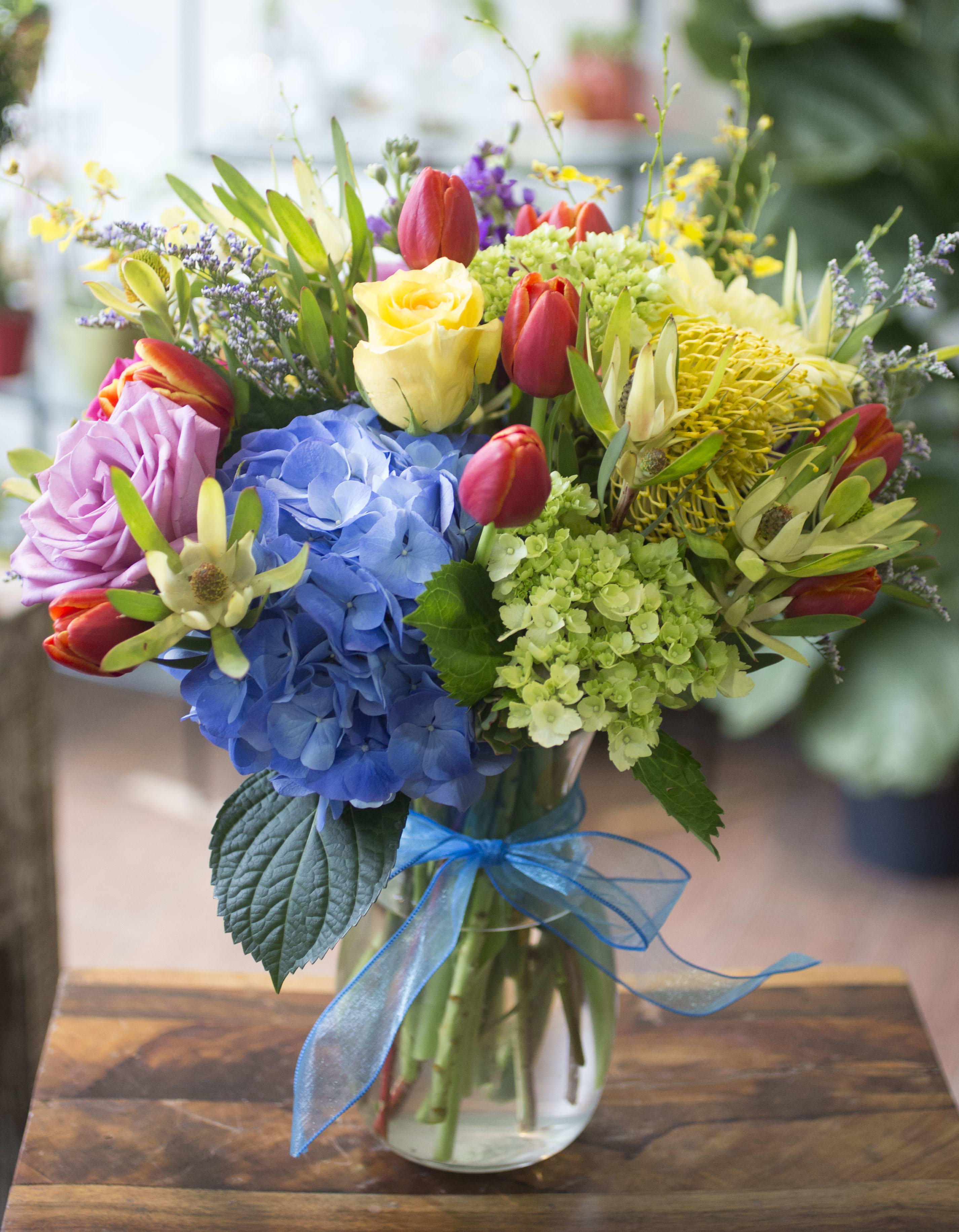 Colorful bouquet of mixed flowers in a glass vase with a blue ribbon