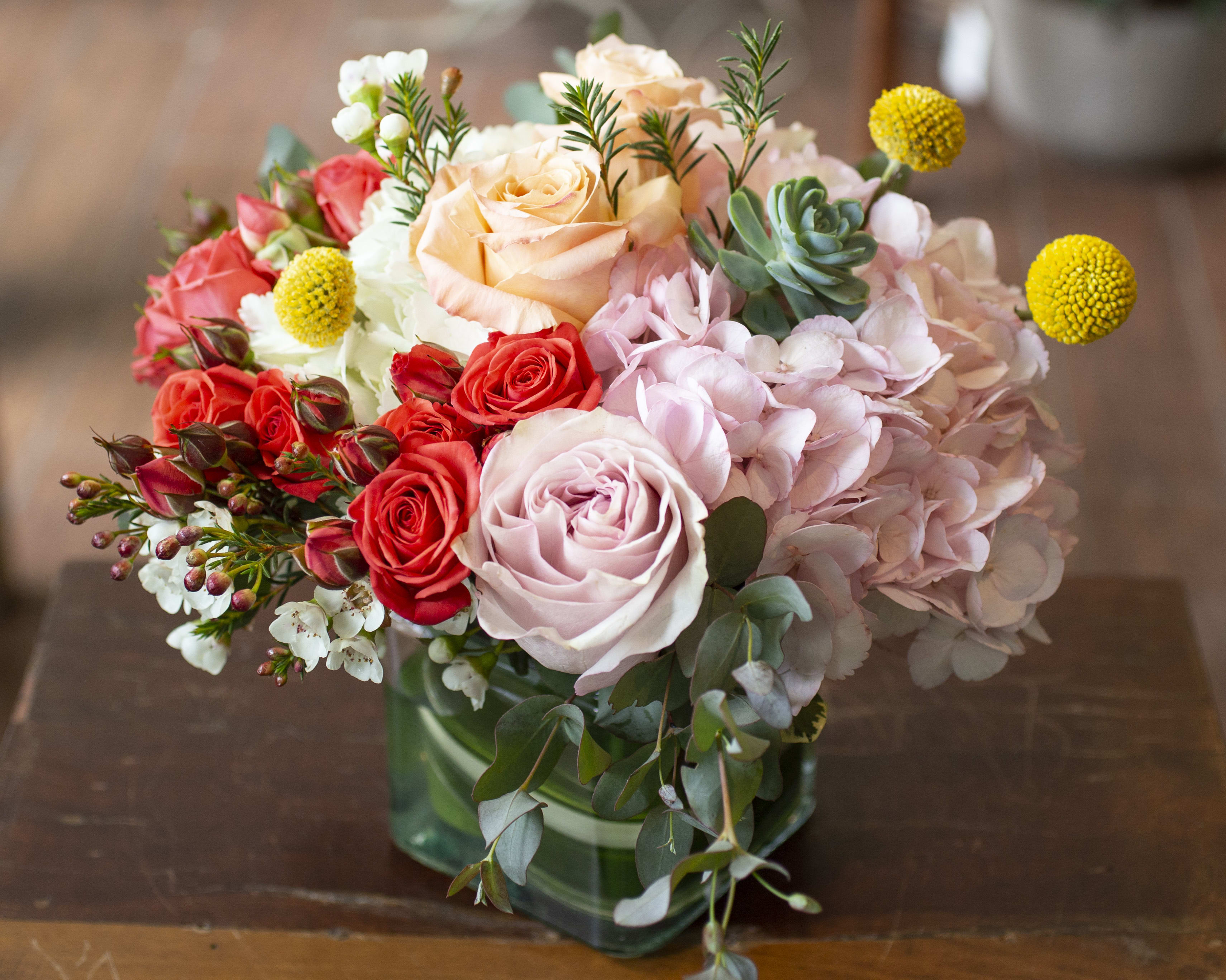 Mixed bouquet of roses, hydrangeas, and succulents in a green glass vase