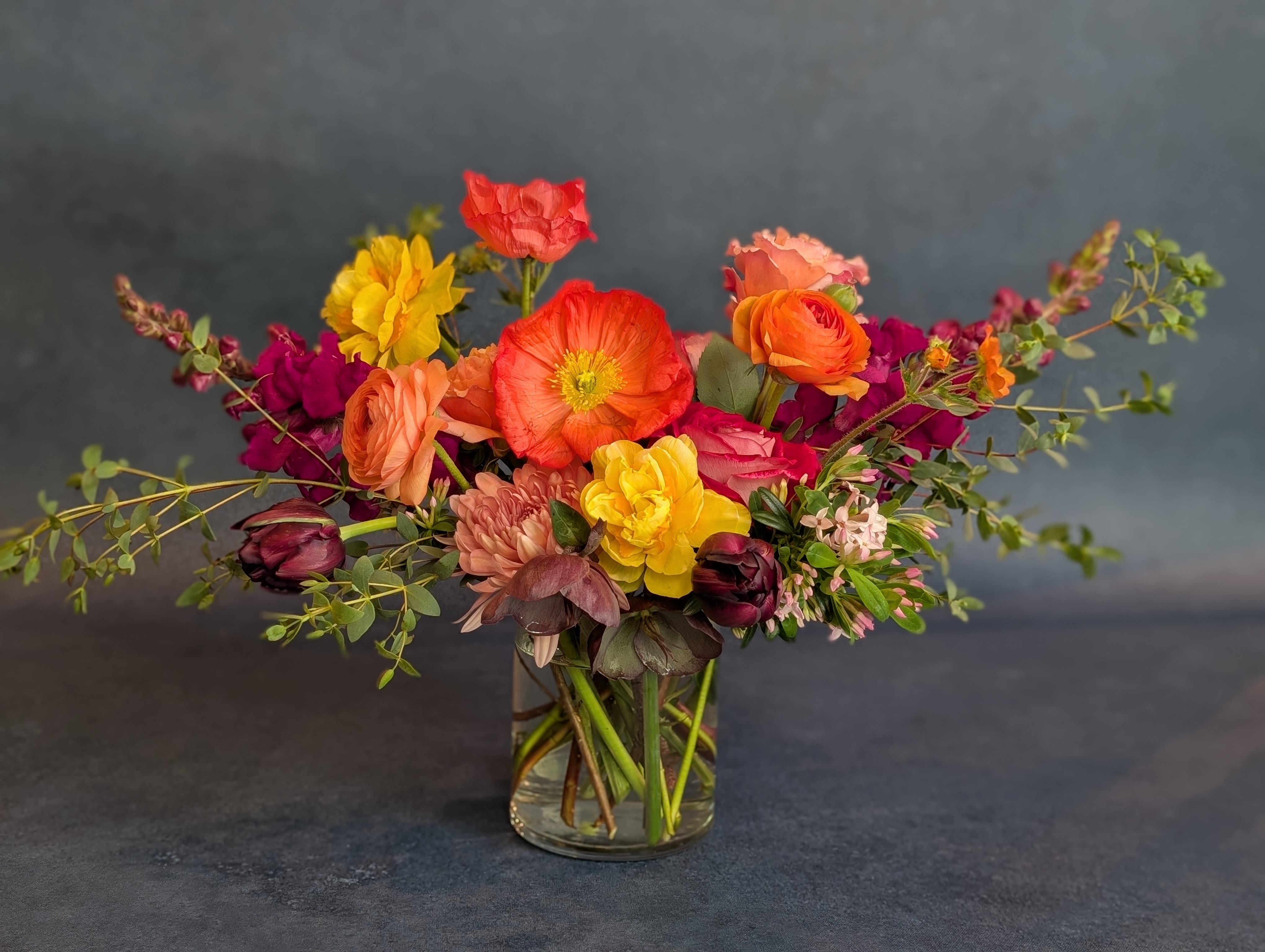 Designer's Choice - Bright &amp; Bold - Bright, garden-fresh color takes center stage in this Designer's Choice - Bright &amp; Bold arrangement. Built in a low, wide clear glass vase for a hand-gathered, garden-style look, it mixes saturated pinks, purples, oranges, yellows and fresh greens for lively texture and movement.    Available in Standard (4" cylinder, about 7-8" tall and 7" wide), Deluxe (5" cylinder, about 10" tall and 10" wide) and Premium (6" cylinder, about 12" tall and 12" wide); colors and varieties may vary seasonally as our designers choose the freshest blooms.