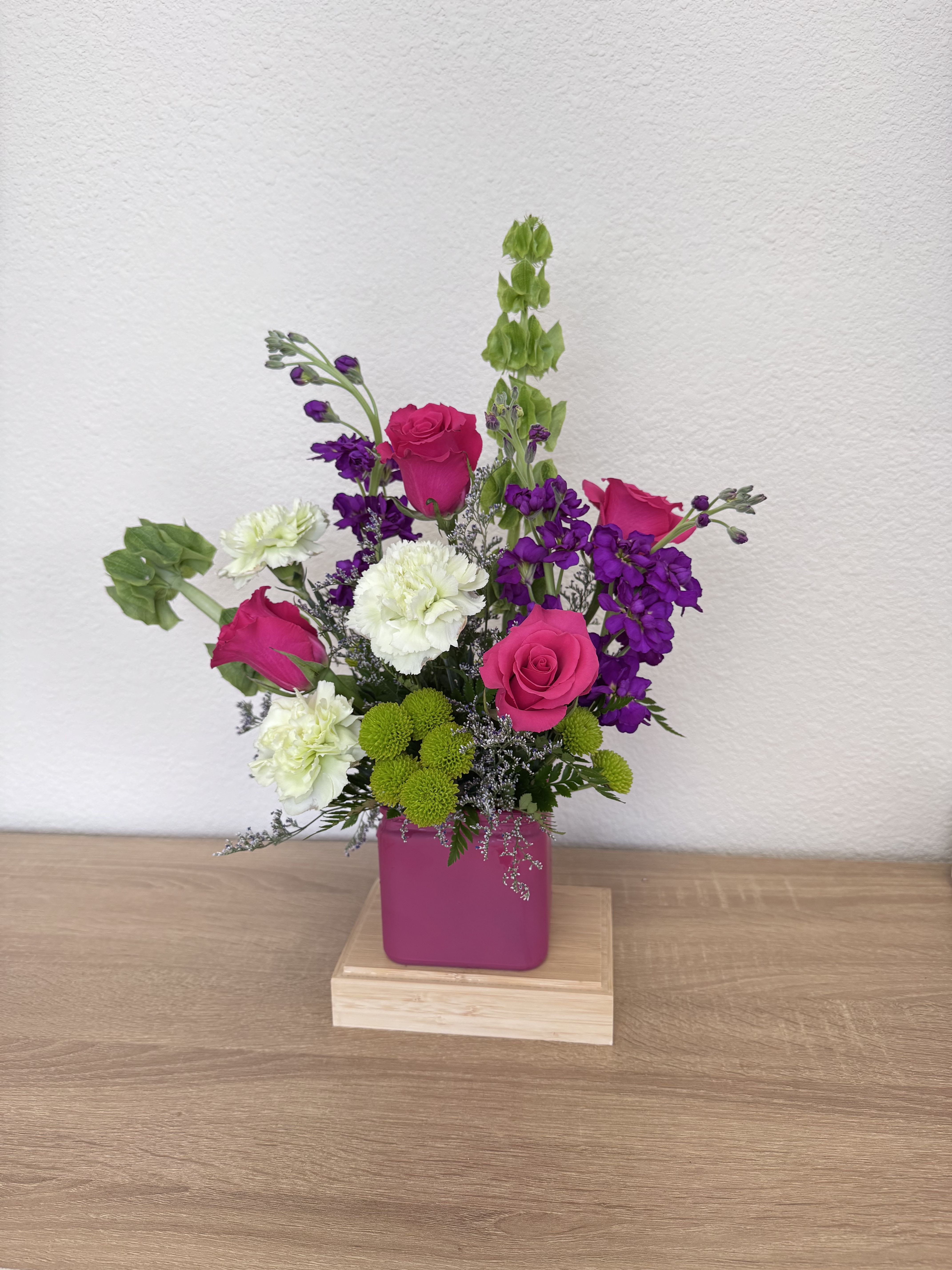 Bold Blooms  - Hot pink roses and vibrant purple stock take center stage in this cheerful flower arrangement, perfect for any special moment. The compact upright design reads bright and lively-the saturated pinks and purples pop against green carnations and pops of green chrysanthemum, creating an energetic yet tender bouquet. 