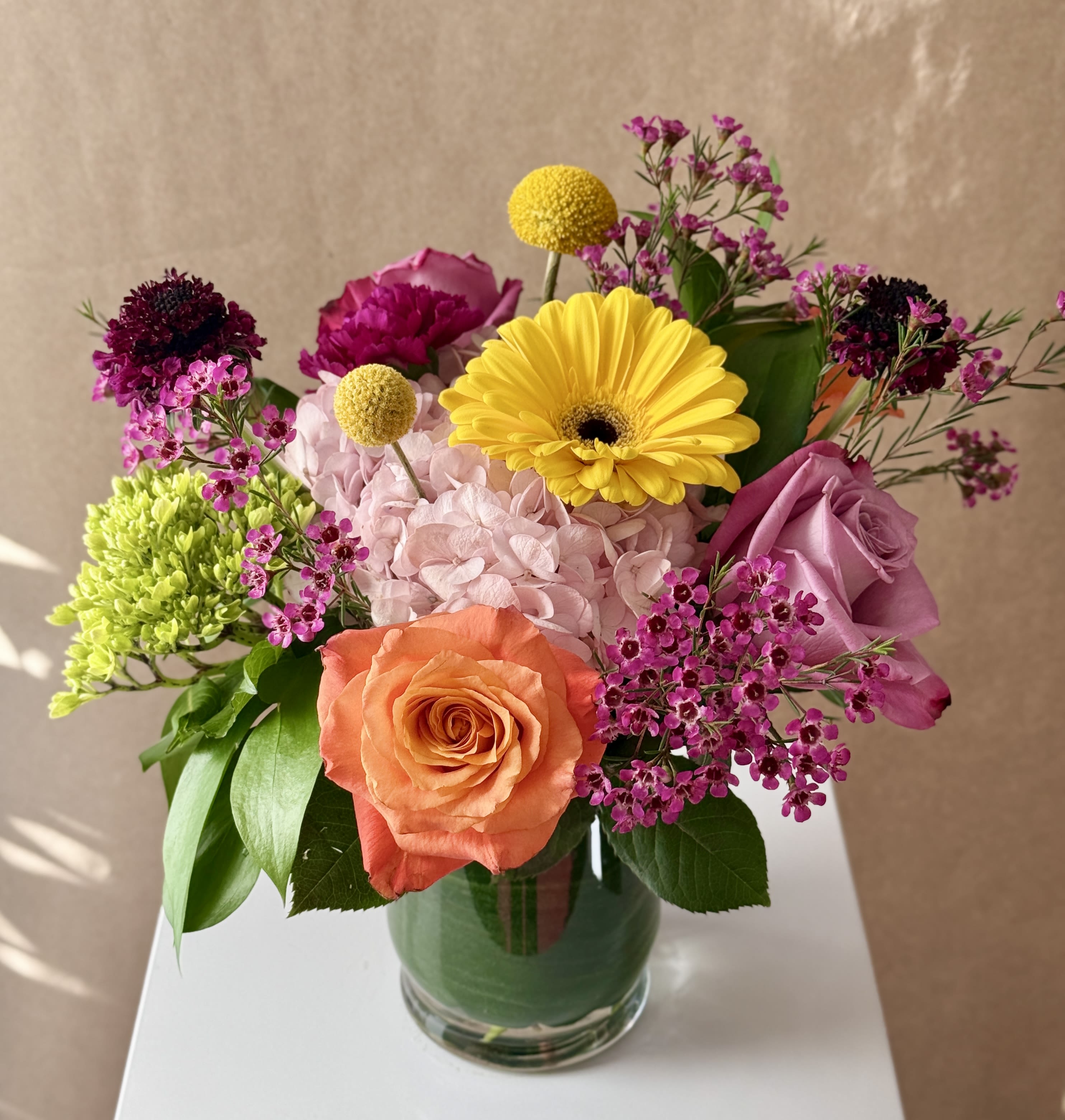 Mixed bouquet in a glass vase with roses, hydrangea, and bright yellow blooms