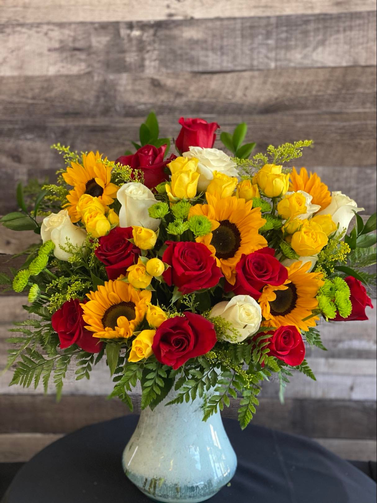 Bouquet of red, yellow, and white roses with sunflowers in a white vase