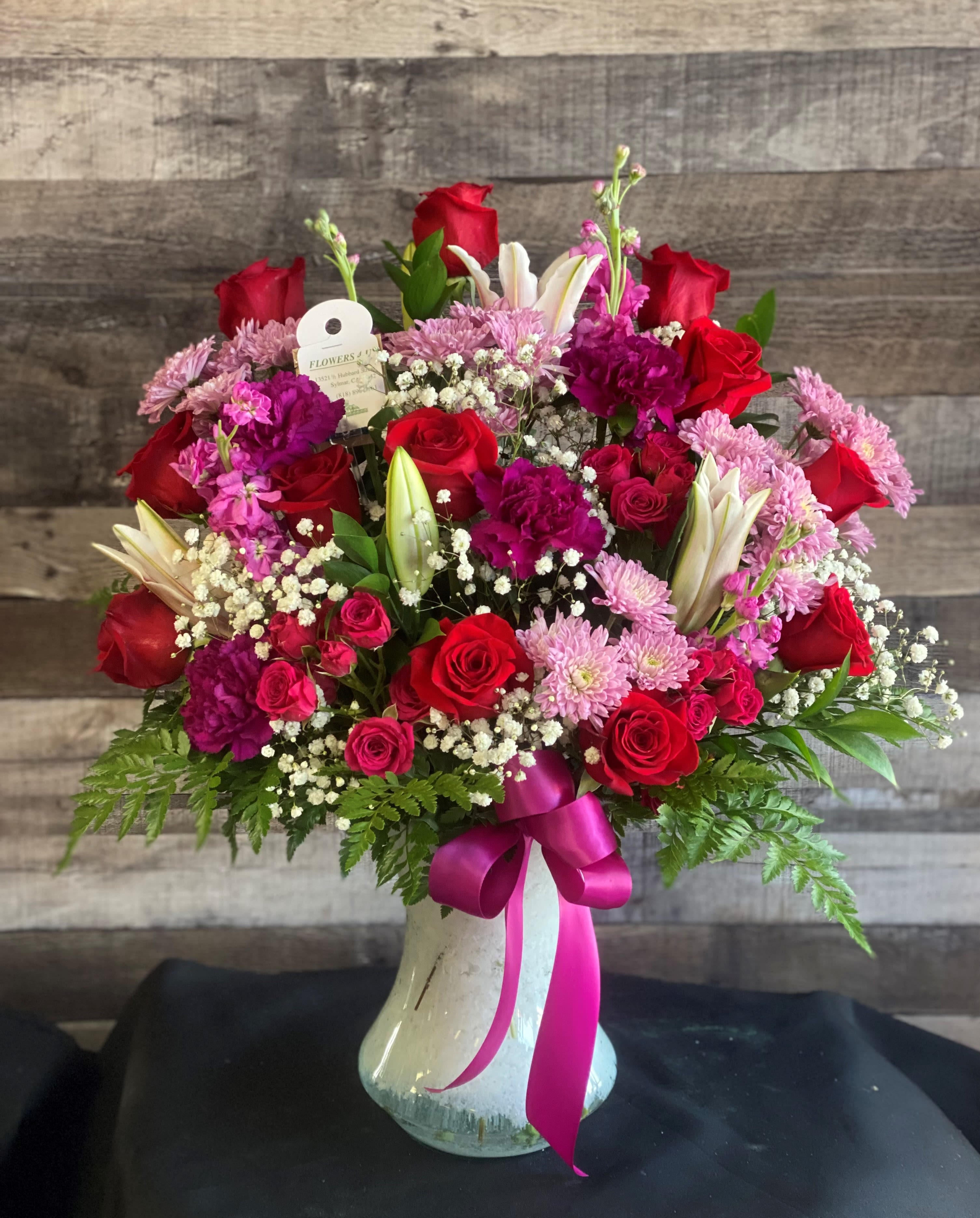 Red and pink mixed flower arrangement in a white vase with a ribbon