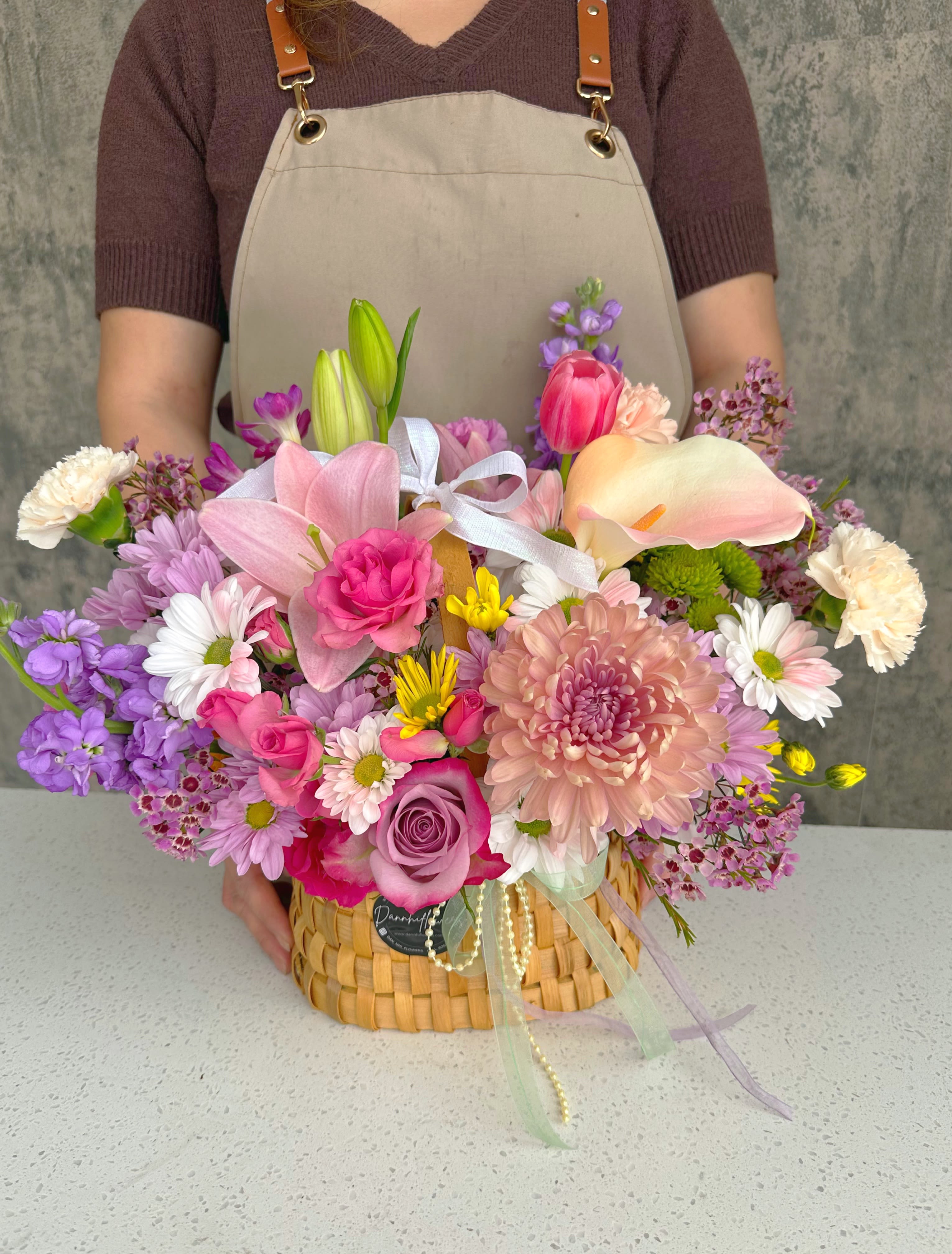 Pastel mixed flower arrangement in a woven basket with ribbon