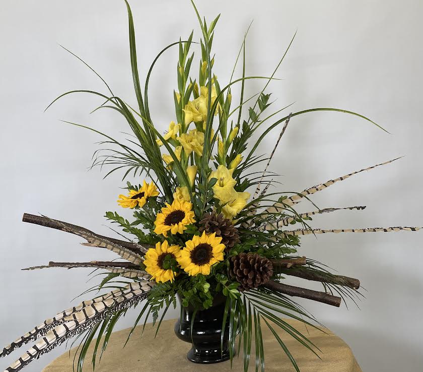 Tall arrangement of yellow flowers and sunflowers in a black vase
