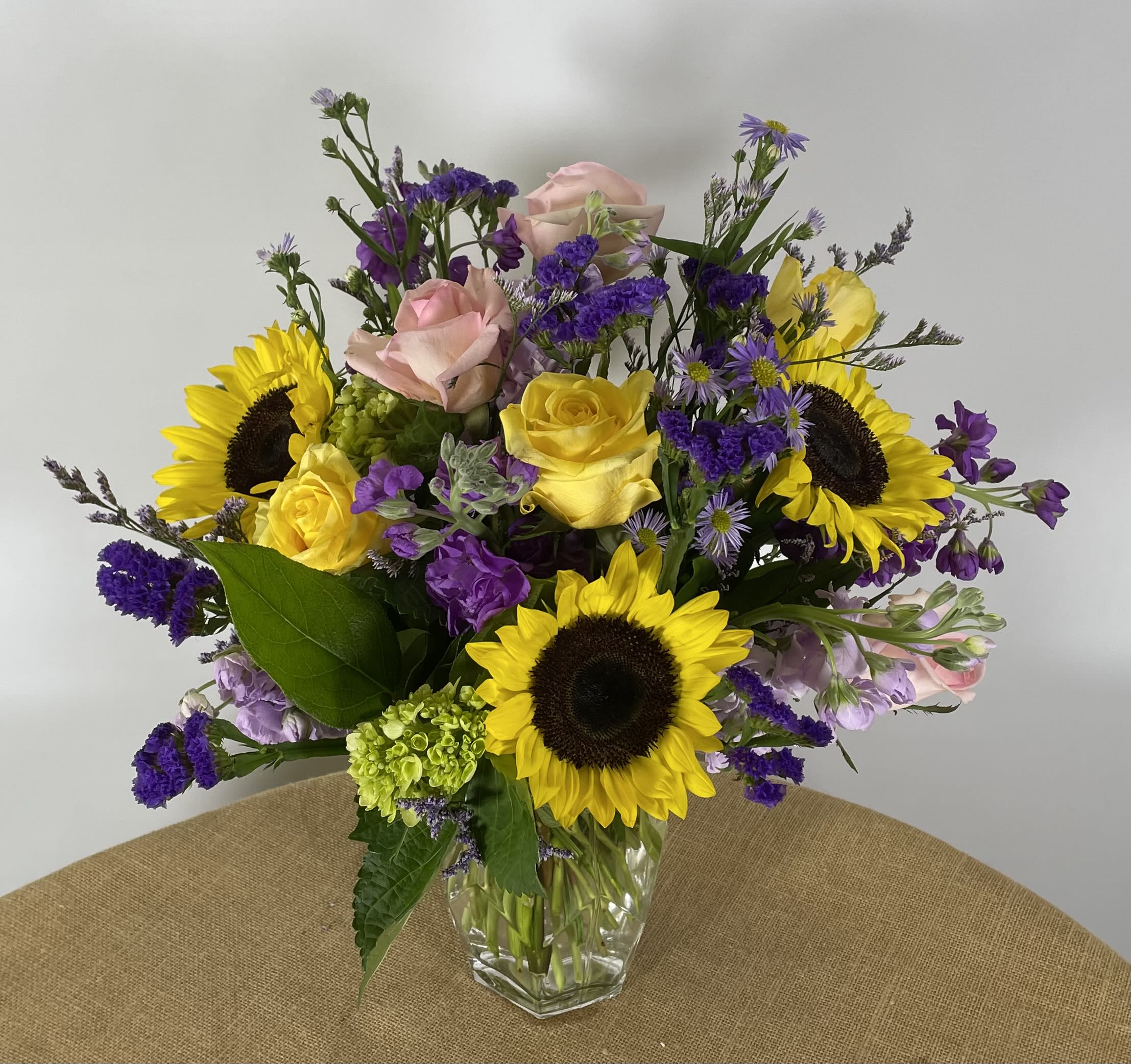 Mixed bouquet of sunflowers, yellow and pink roses in a clear glass vase