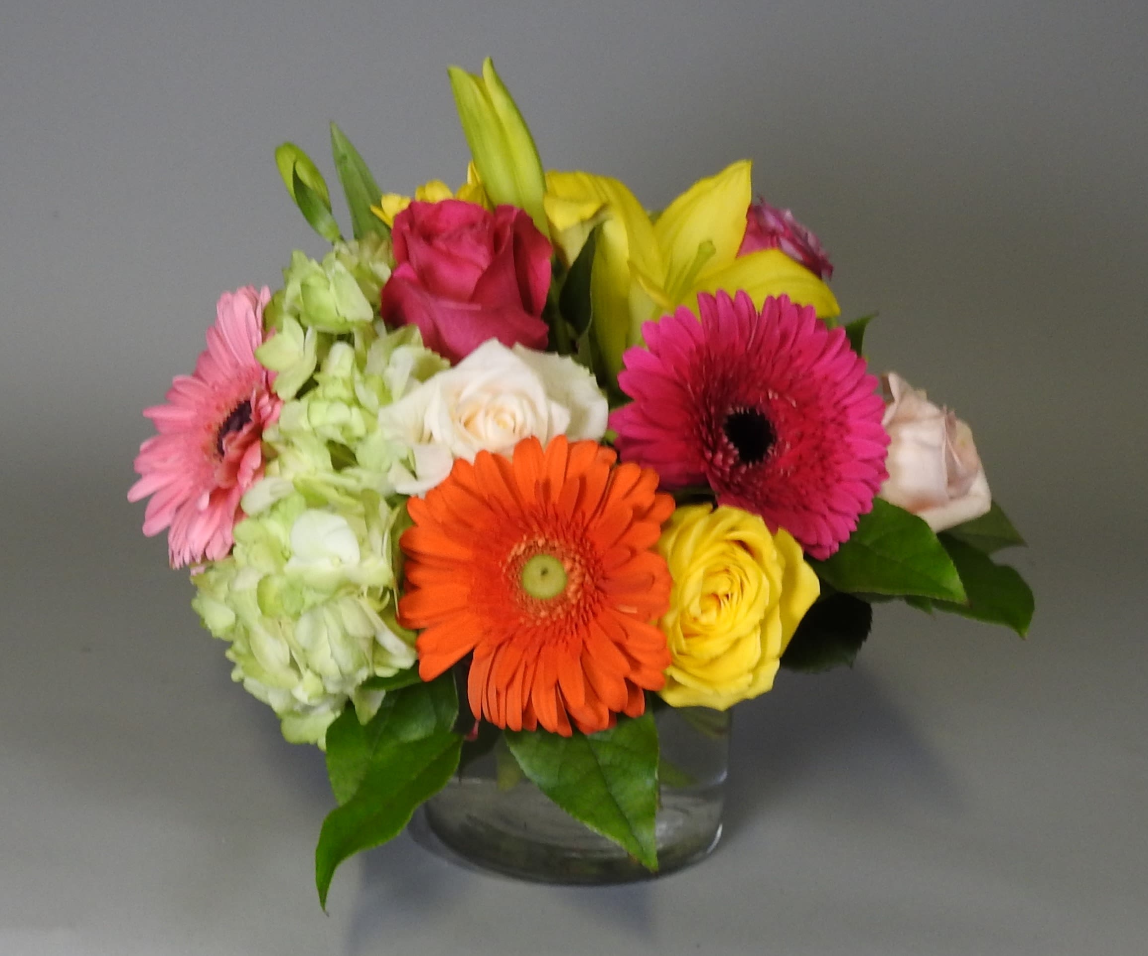 Mixed bouquet of gerbera daisies, roses, lilies, and hydrangea in a glass vase
