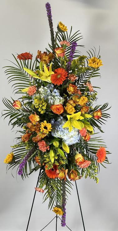 Tall standing floral spray with mixed bright flowers on a black easel