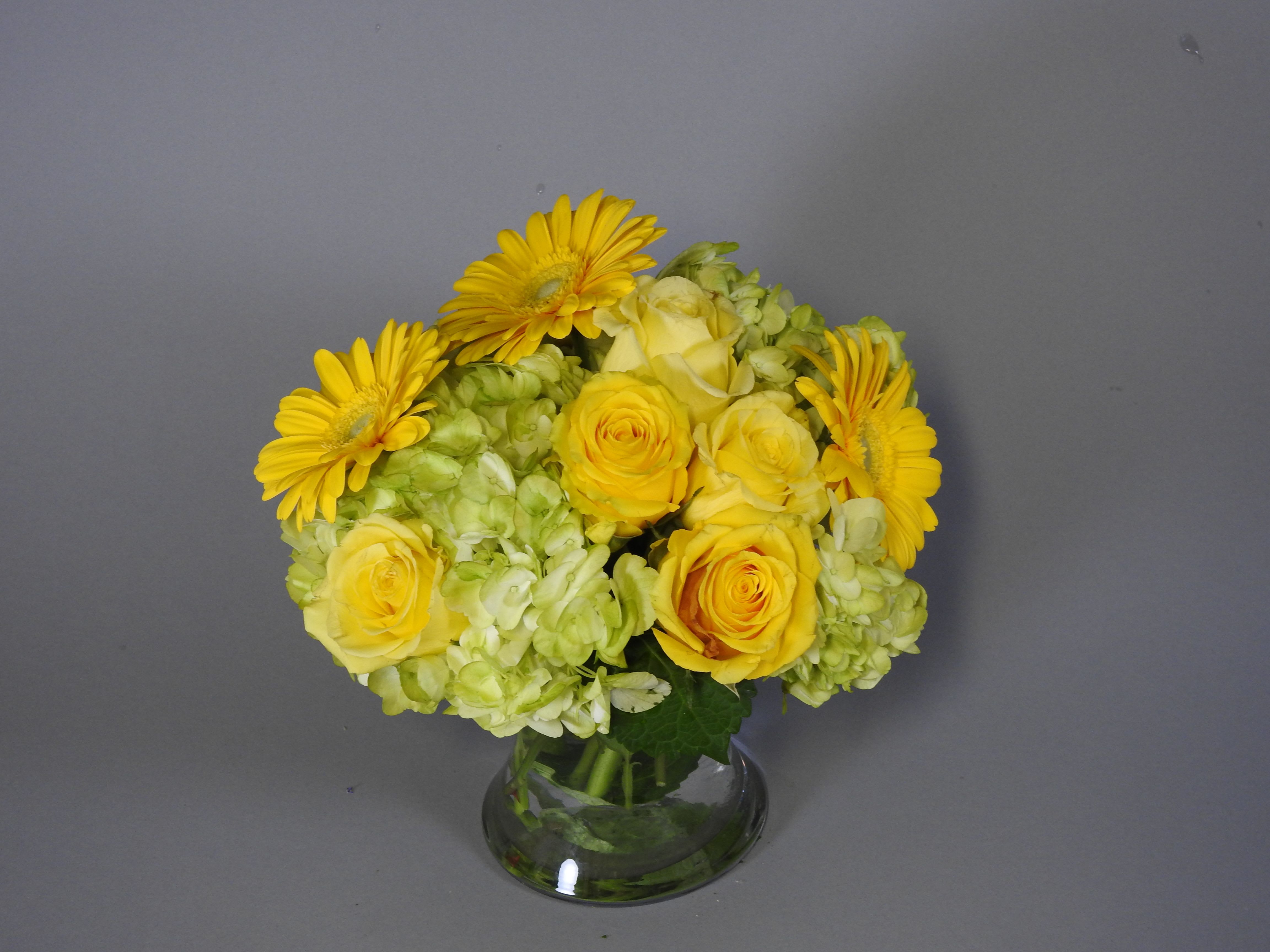 Yellow roses and gerbera daisies in a clear glass vase