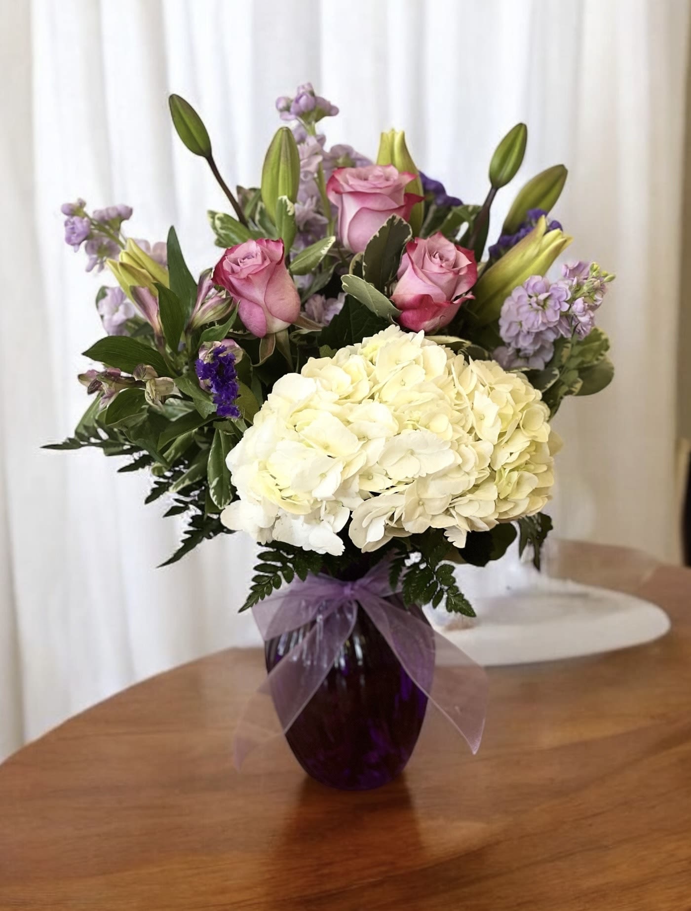 Bouquet of pink roses, white hydrangea, and purple flowers in a vase