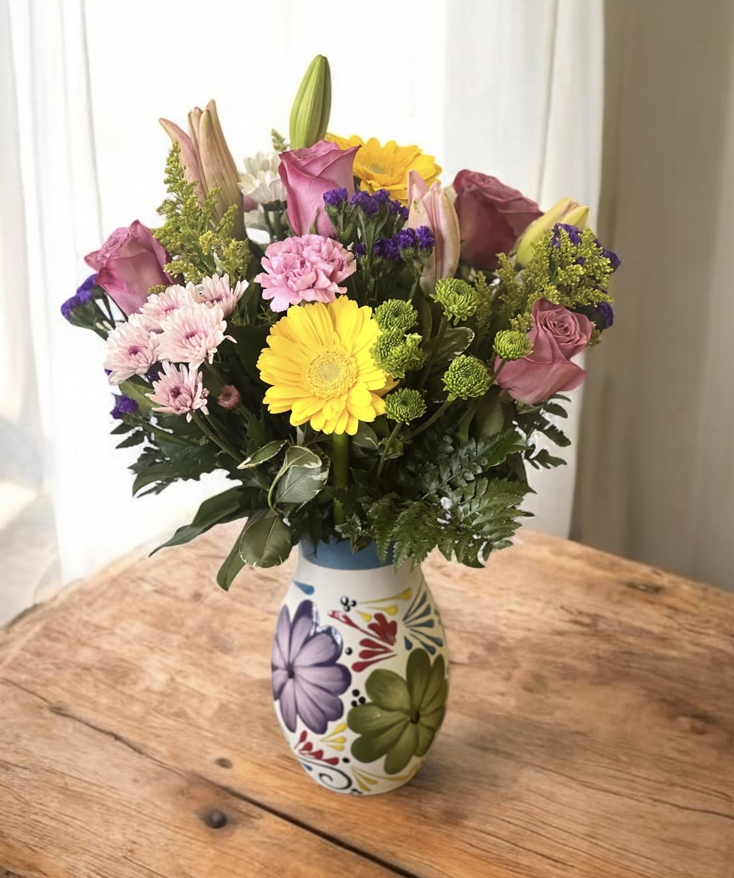 Mixed bouquet in a painted ceramic vase with pink, yellow, and purple flowers.