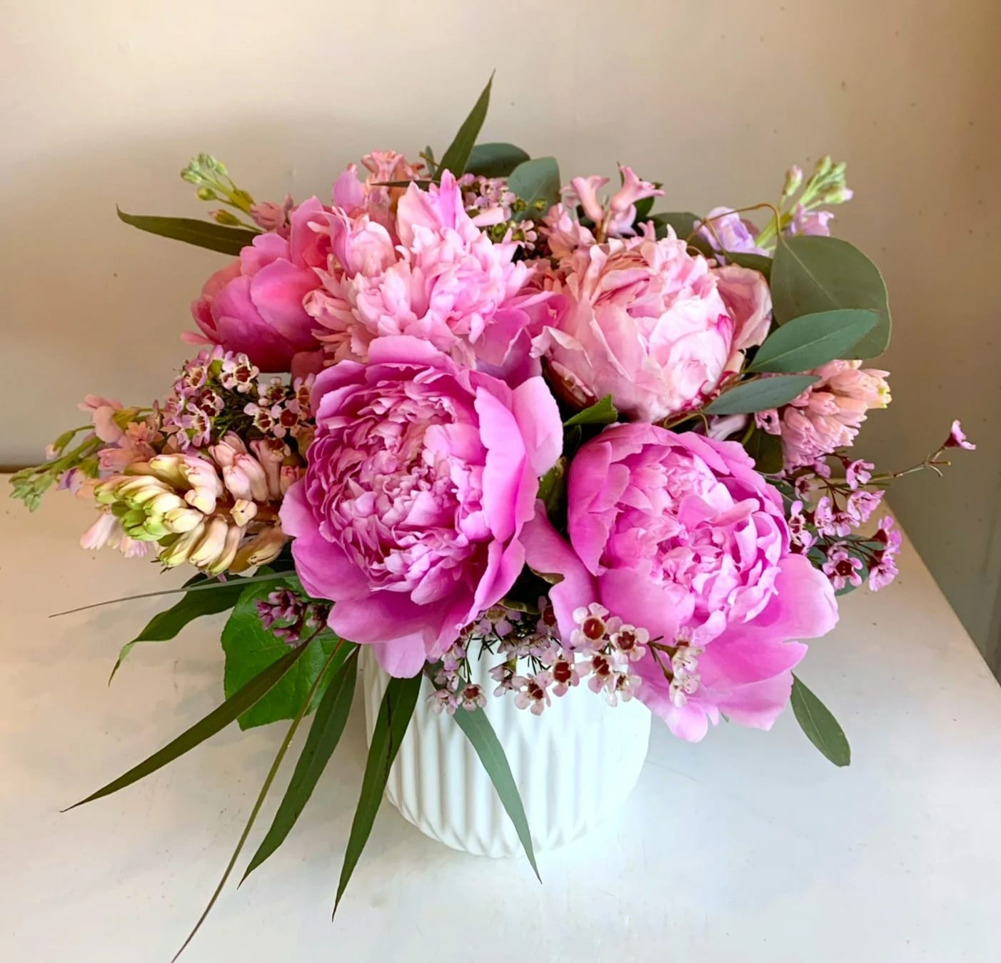 Pink peonies and small pink flowers arranged in a white vase