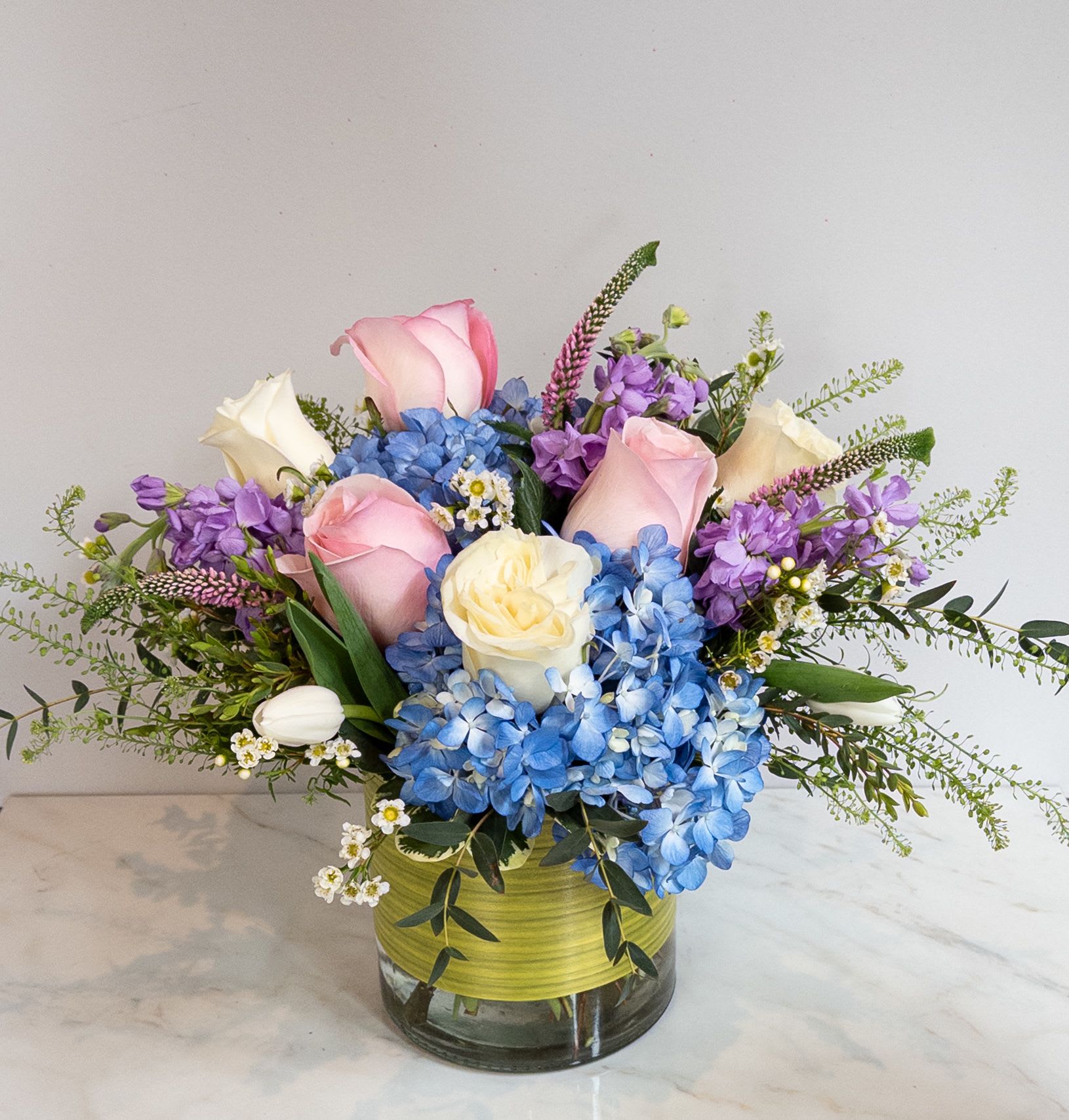 Pink and white roses with blue hydrangeas in a glass vase
