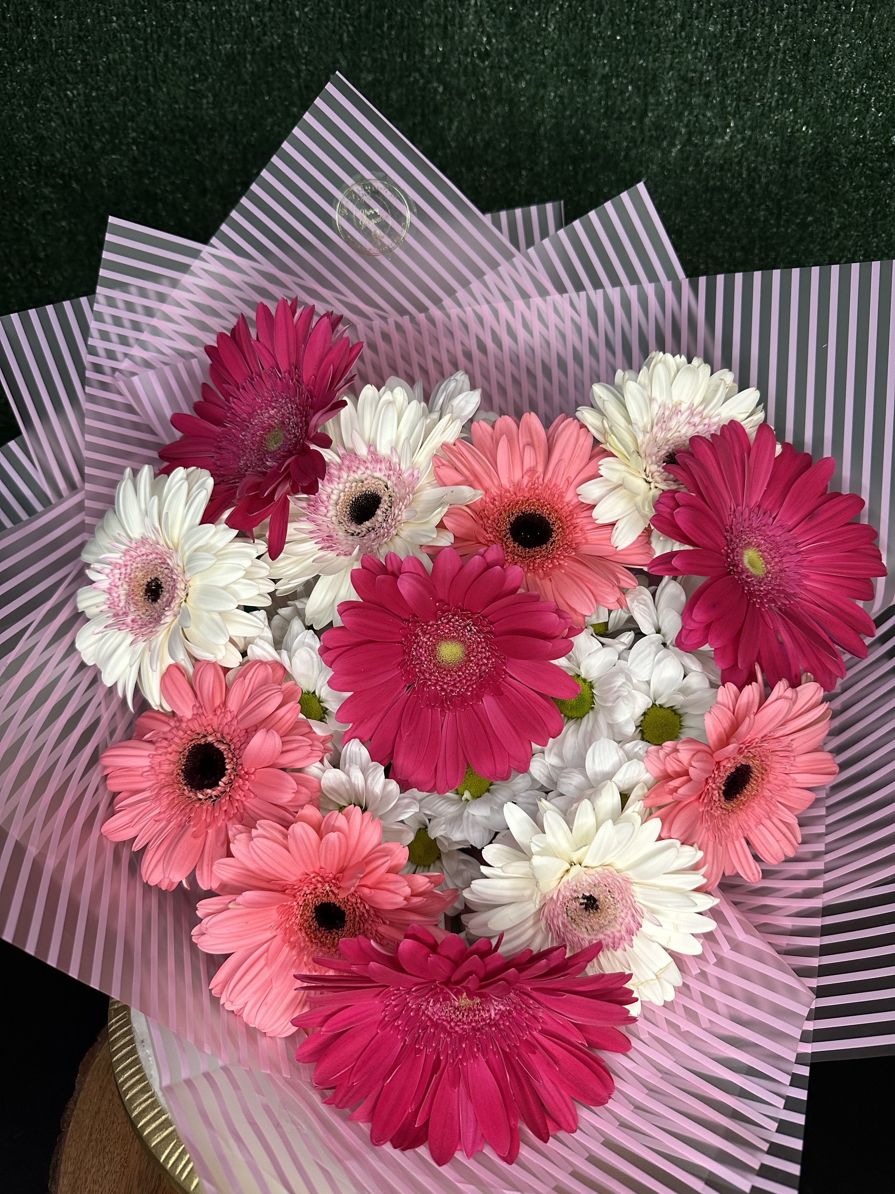 Bouquet of pink, white, and coral gerbera daisies wrapped in striped paper