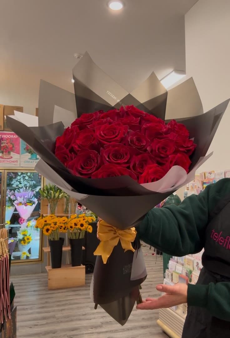 Bouquet of red roses wrapped in black paper with a gold ribbon