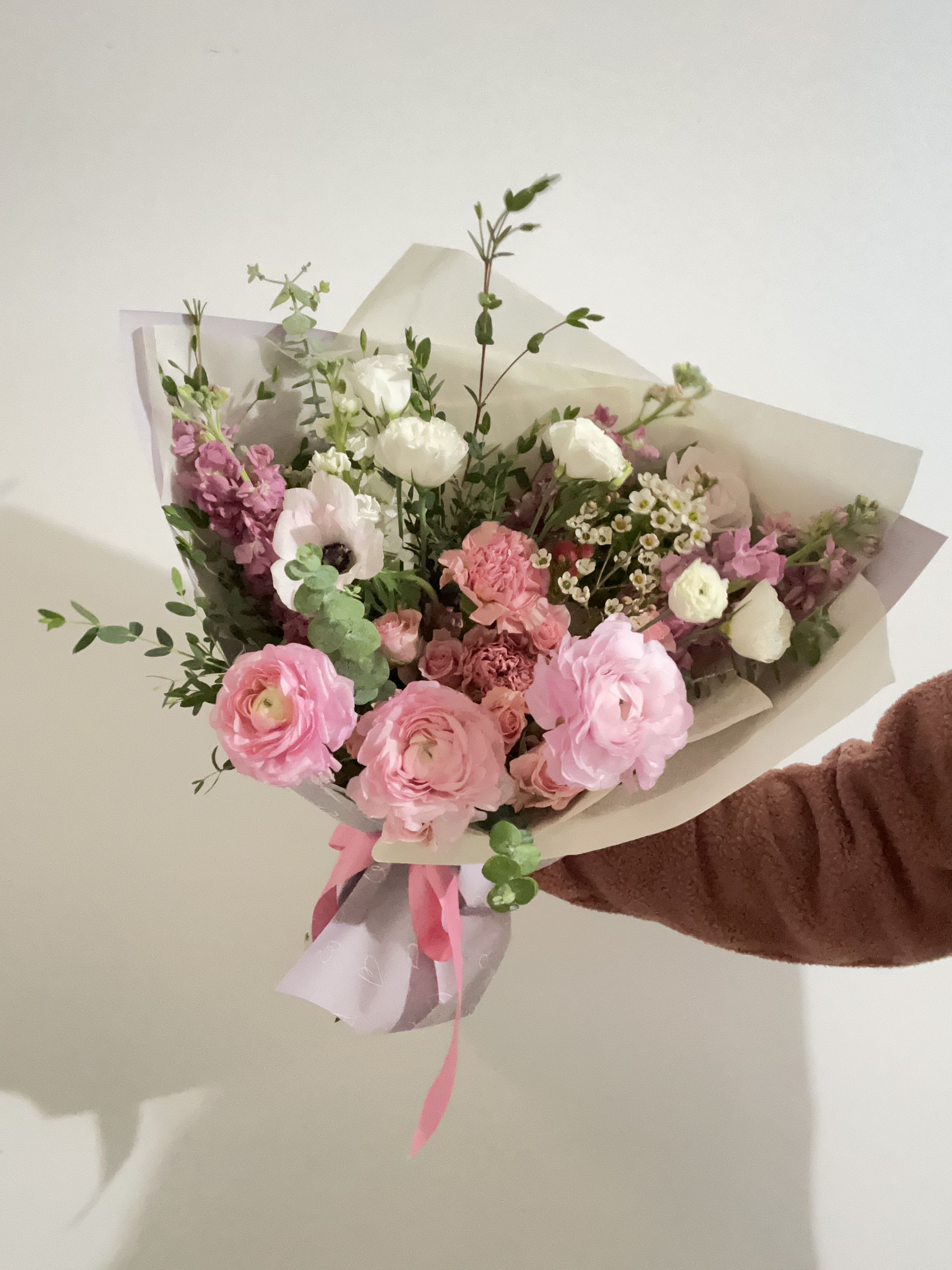 Handheld bouquet of pink and white flowers wrapped in paper