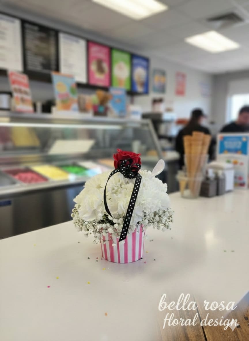 White floral arrangement in a pink striped container with a red rose topper