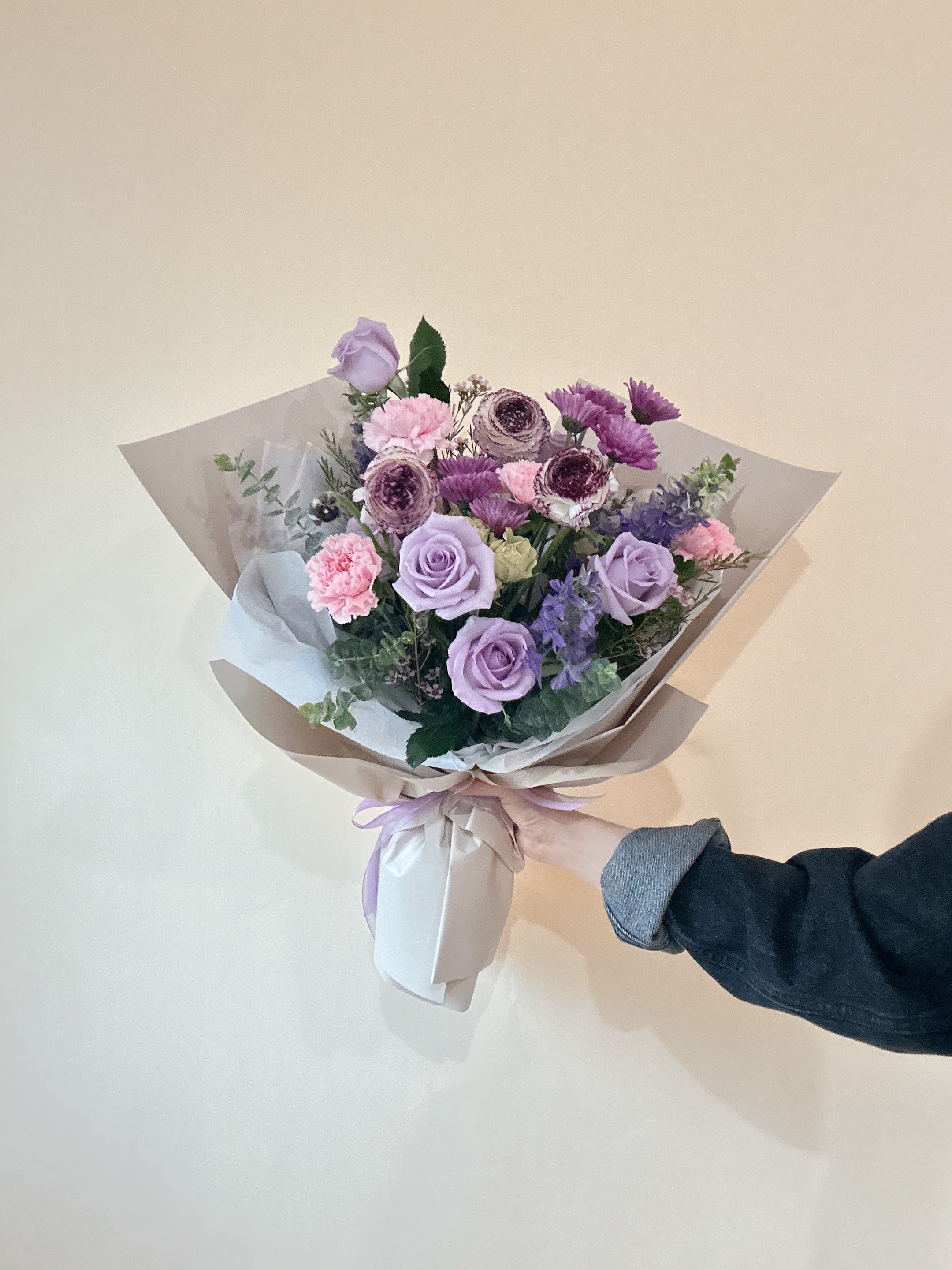Hand-tied bouquet of lavender roses and pink flowers wrapped in paper