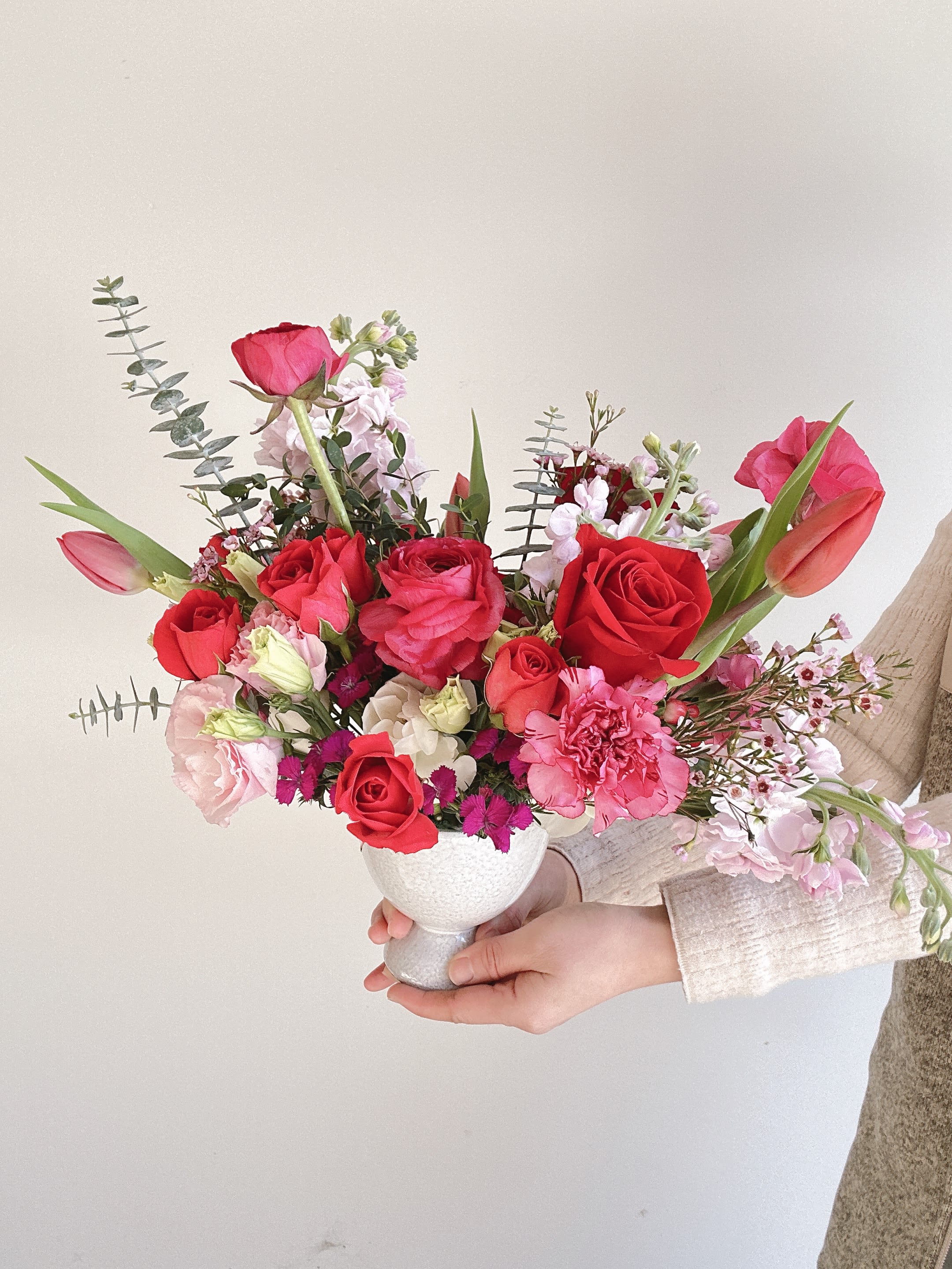 Handheld bouquet of red and pink flowers in a white vase