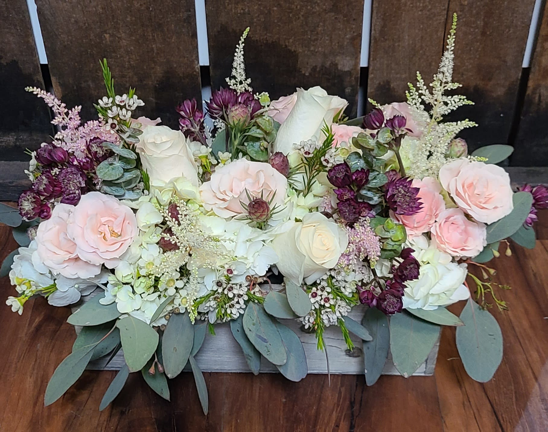 Winery vibes - This low, rectangular design is great for a centerpiece at a special occasion or any day you want to brighten someone’s day. The design comes in a wooden box and features a variety of foliage with delicate pink and white accents.