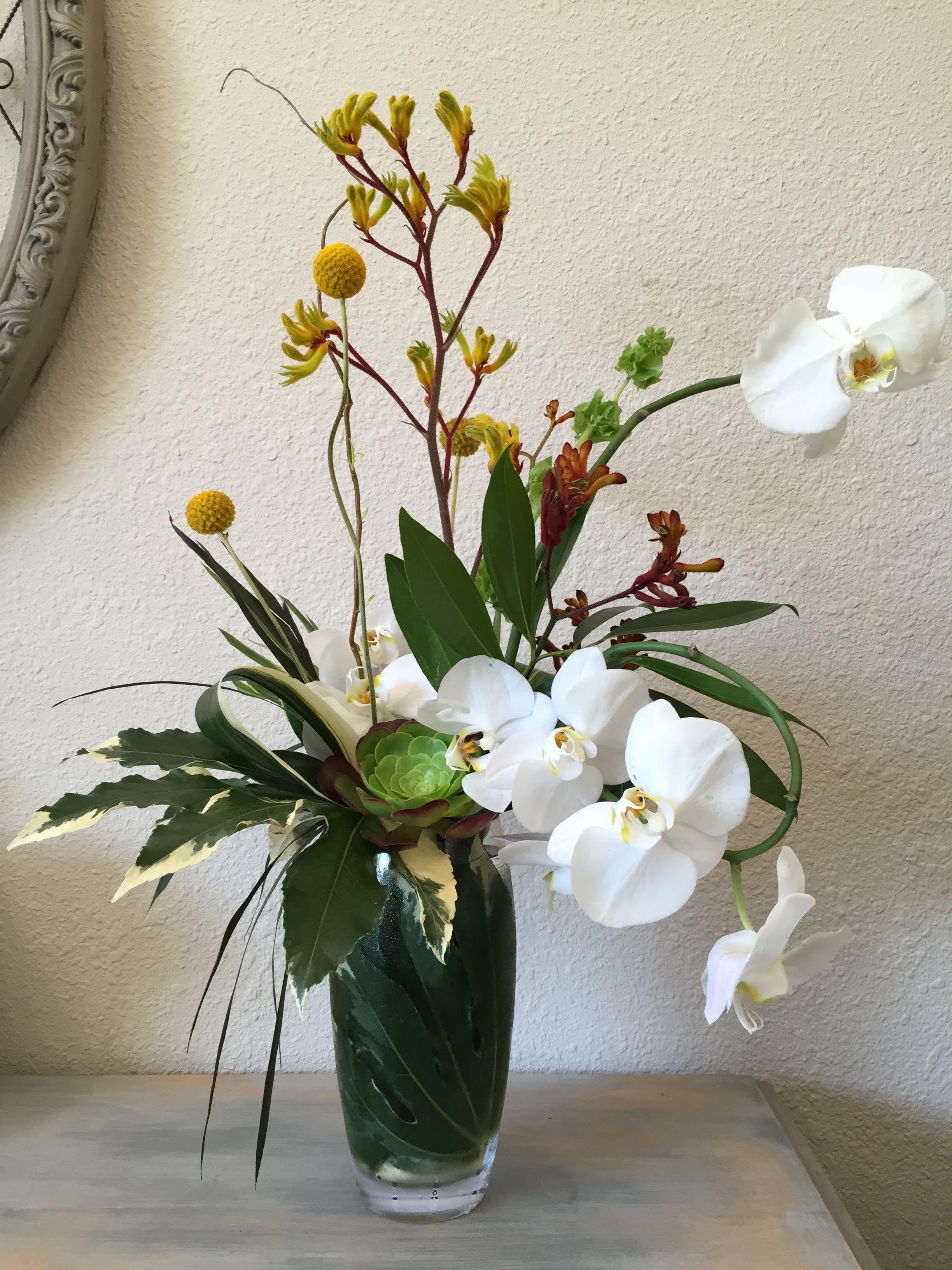 White orchids and yellow accent flowers in a glass vase