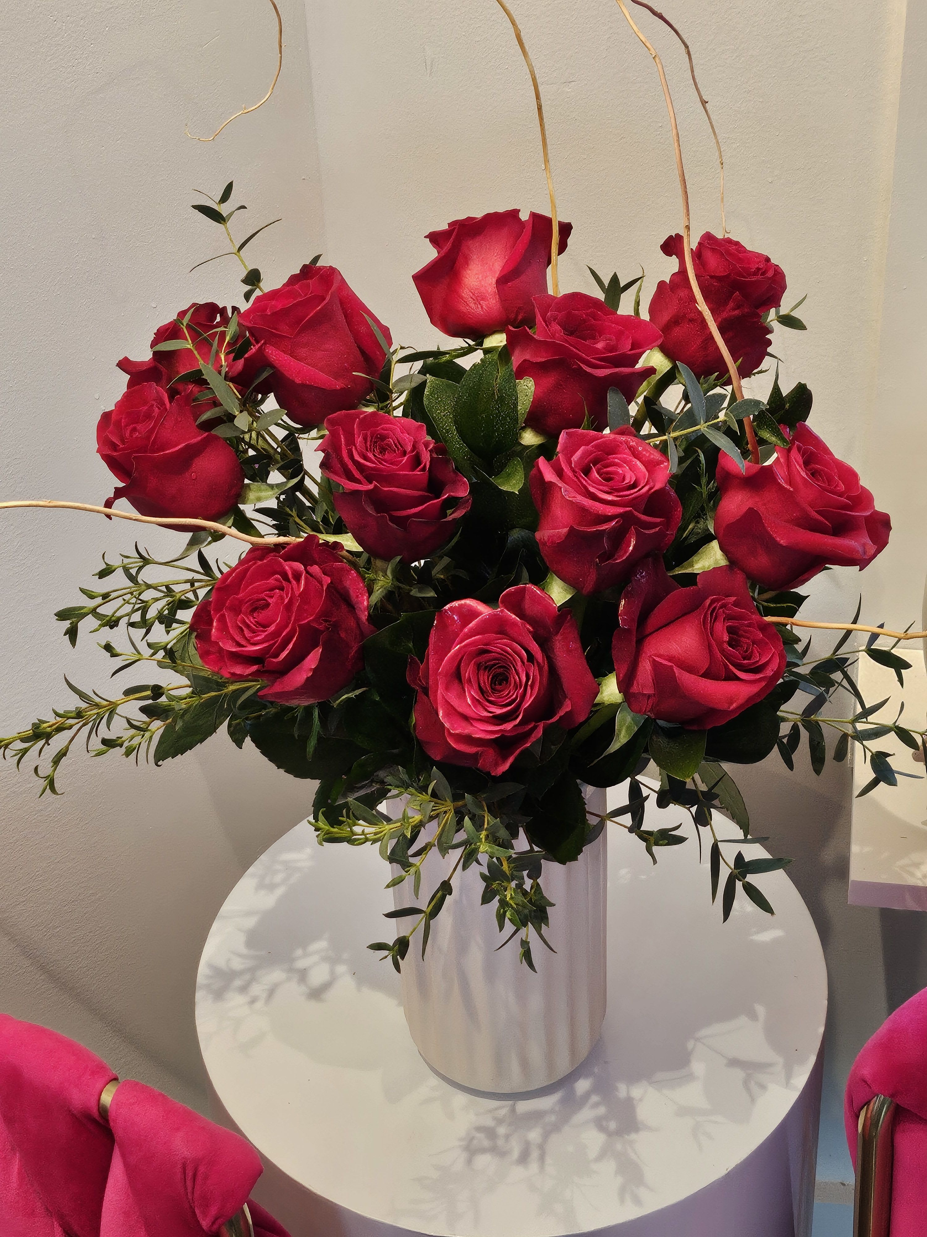 Red roses arranged in a white vase with greenery