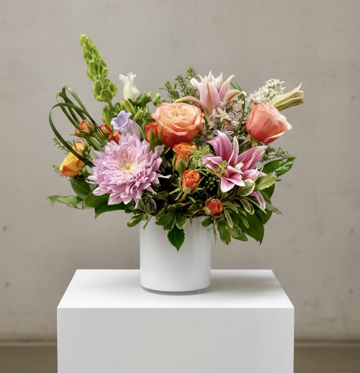 Mixed bouquet of pink, peach, and lavender flowers in a white vase