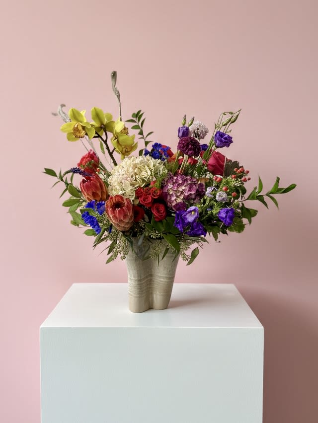 Colorful mixed flower arrangement in a beige vase on a white pedestal