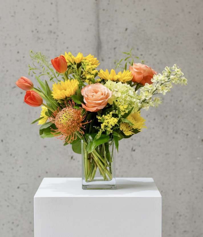 Mixed bouquet in a clear glass vase with orange, yellow, and peach flowers