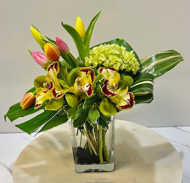 Tropical bouquet with tulips, orchids, and hydrangea in a clear vase