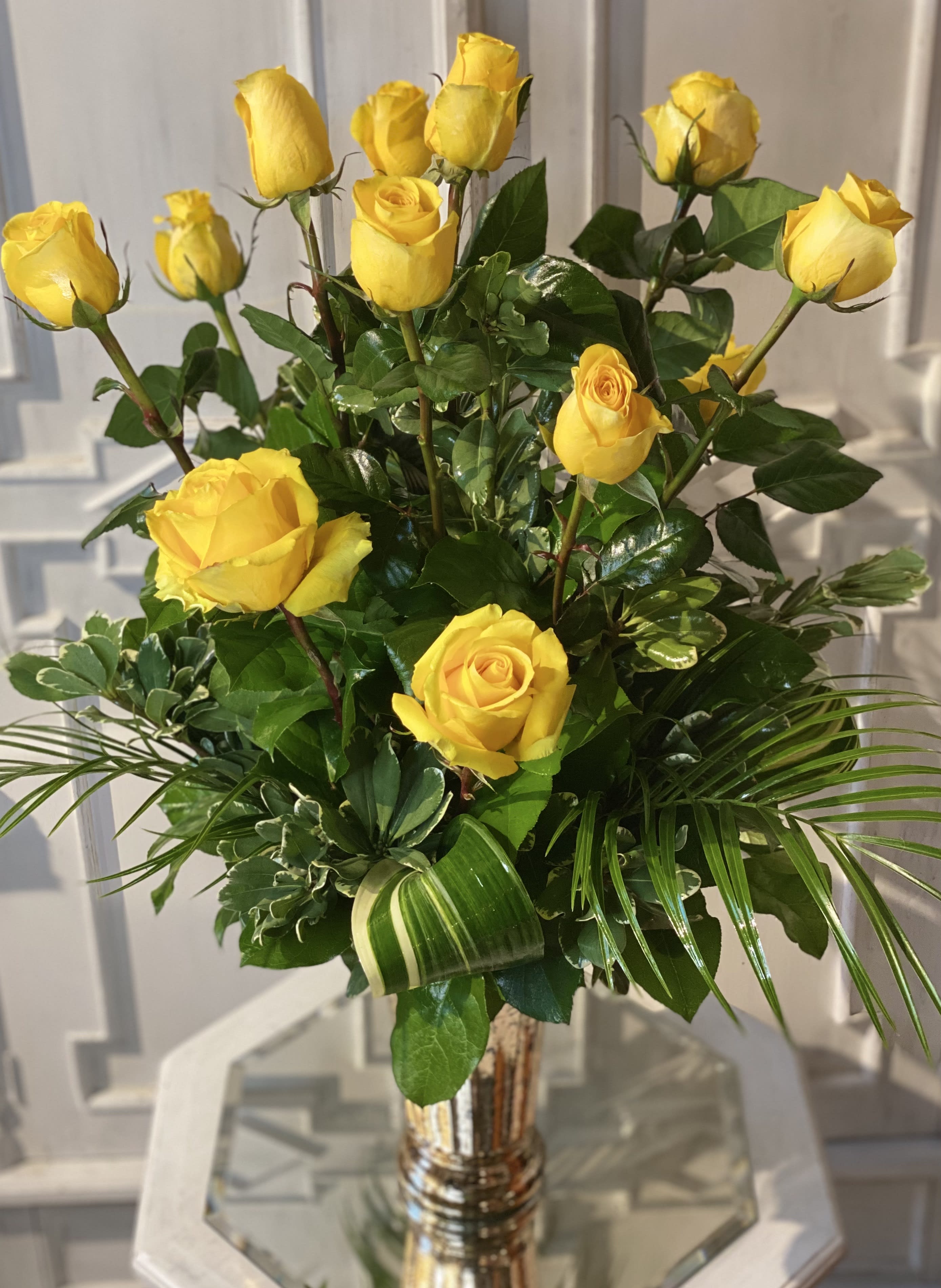 Yellow roses arranged in a clear glass vase with glossy greenery