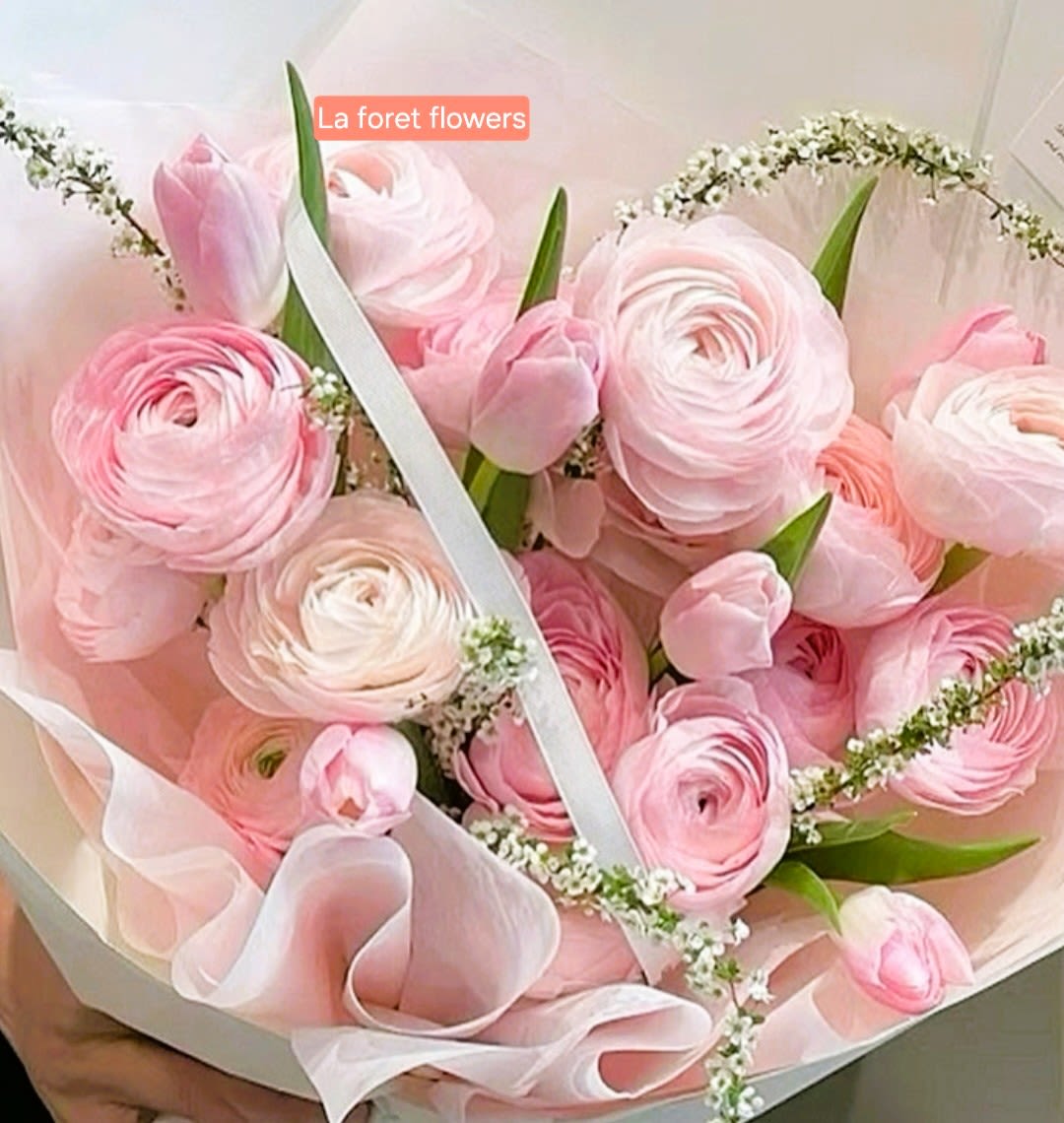 Pink ranunculus bouquet wrapped in pale pink paper with a white ribbon