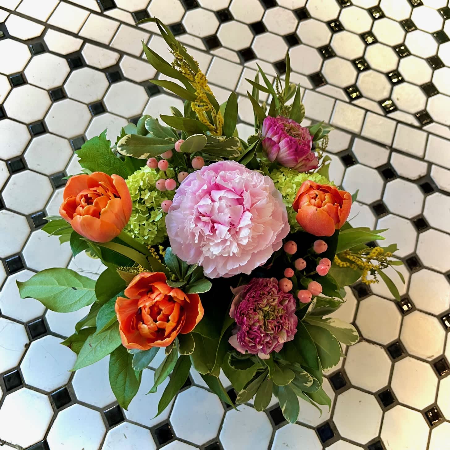 Bouquet of pink and orange flowers with greenery on a tiled floor