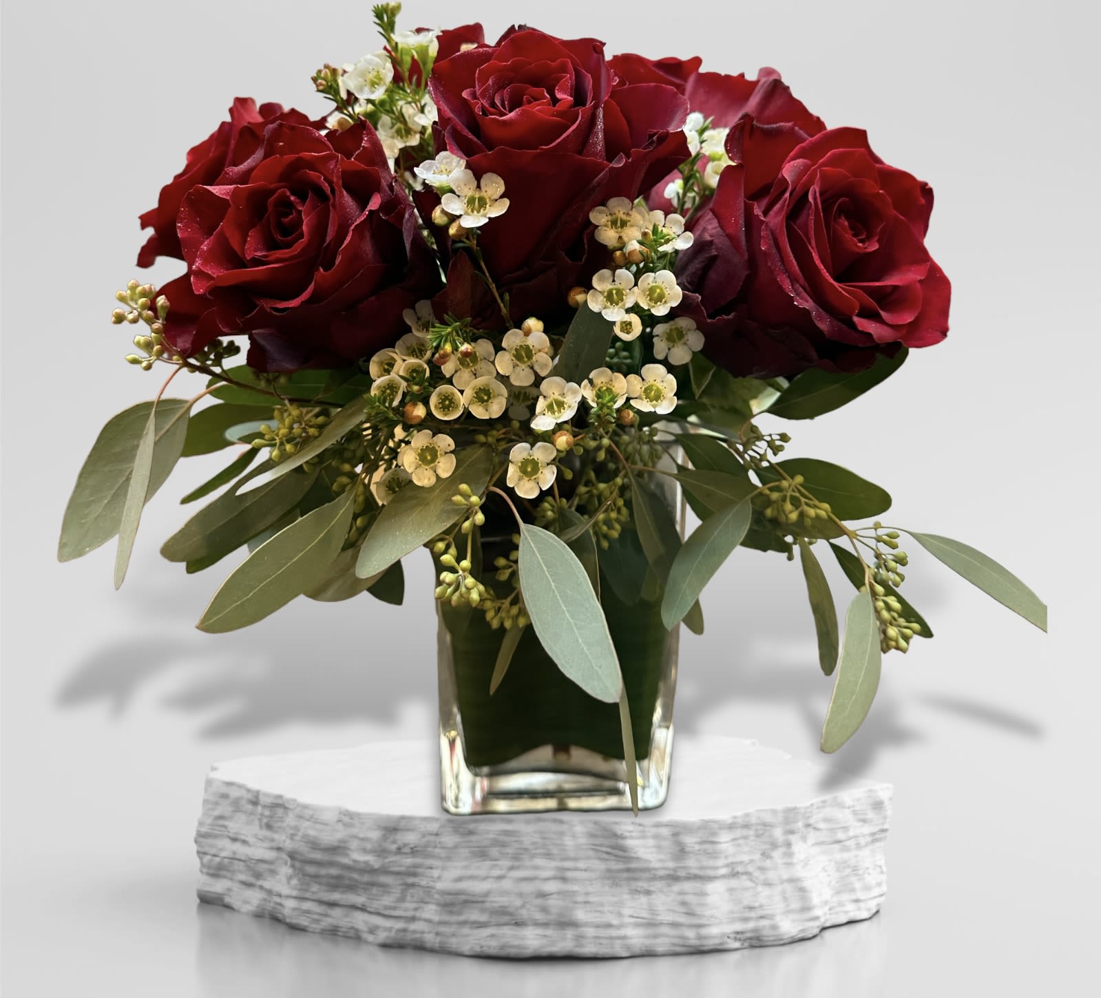 Red roses in a glass vase with small white filler flowers