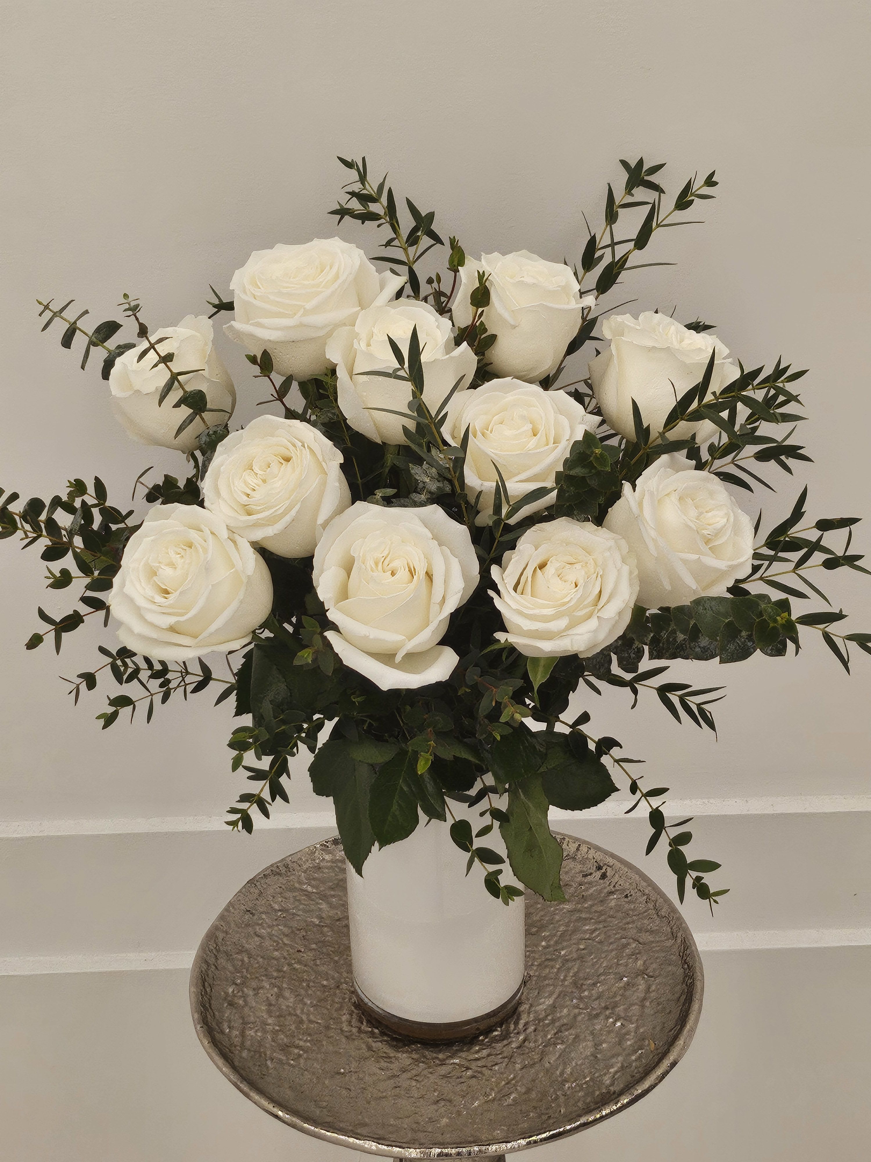 White roses arranged in a white vase with dark greenery
