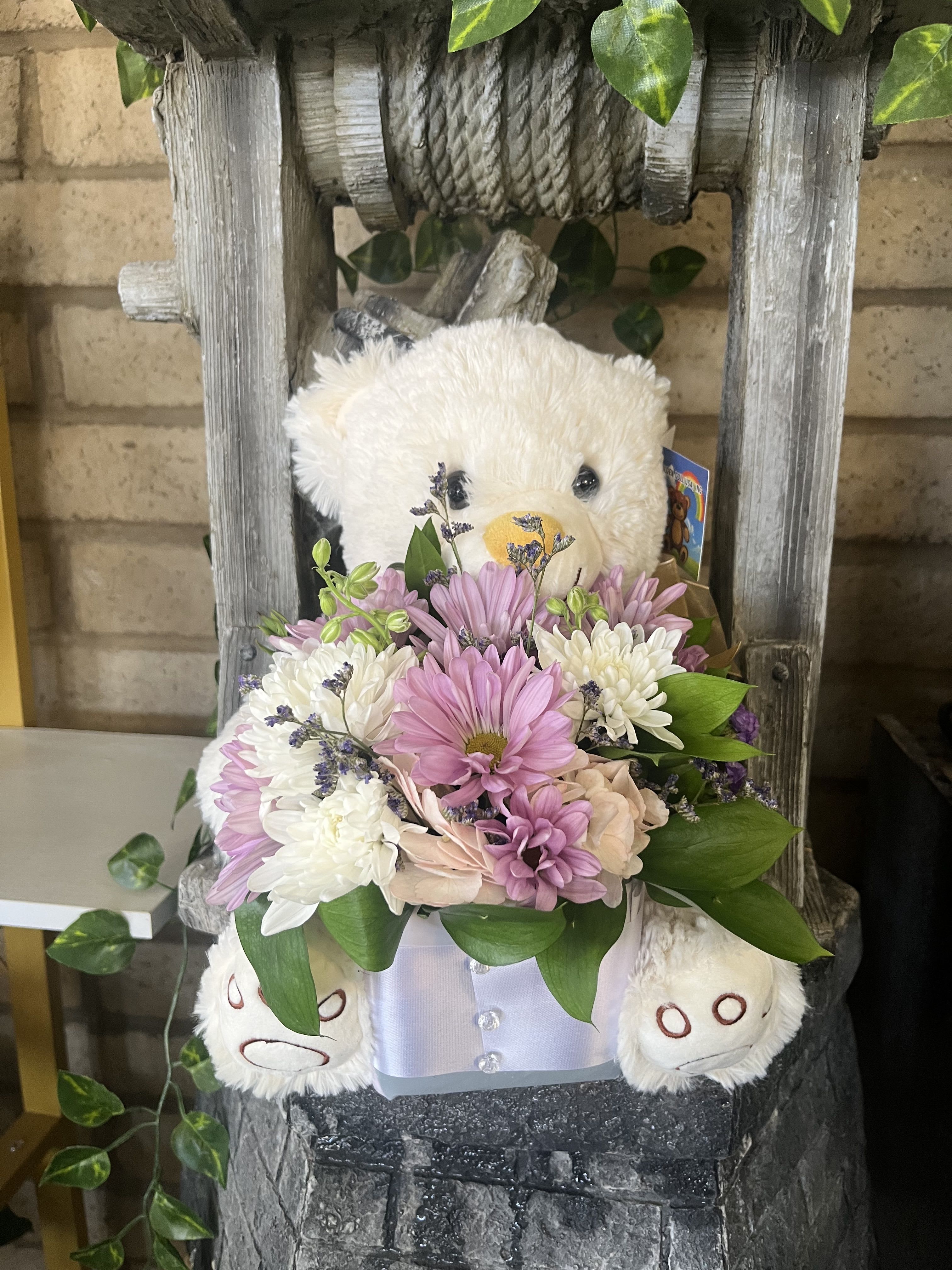 Teddy bear holding a pastel flower arrangement in a box