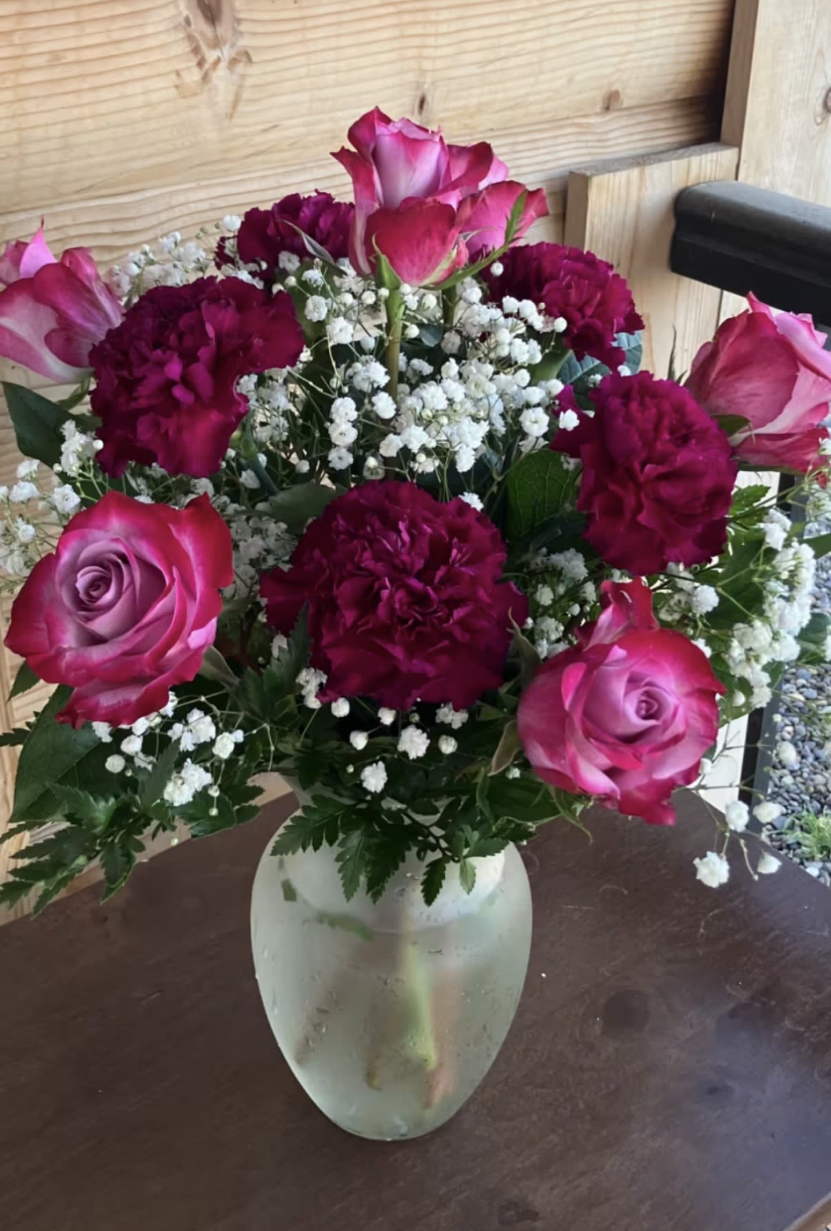 Arrangement of pink roses, deep red carnations, and white filler flowers in a frosted glass vase.